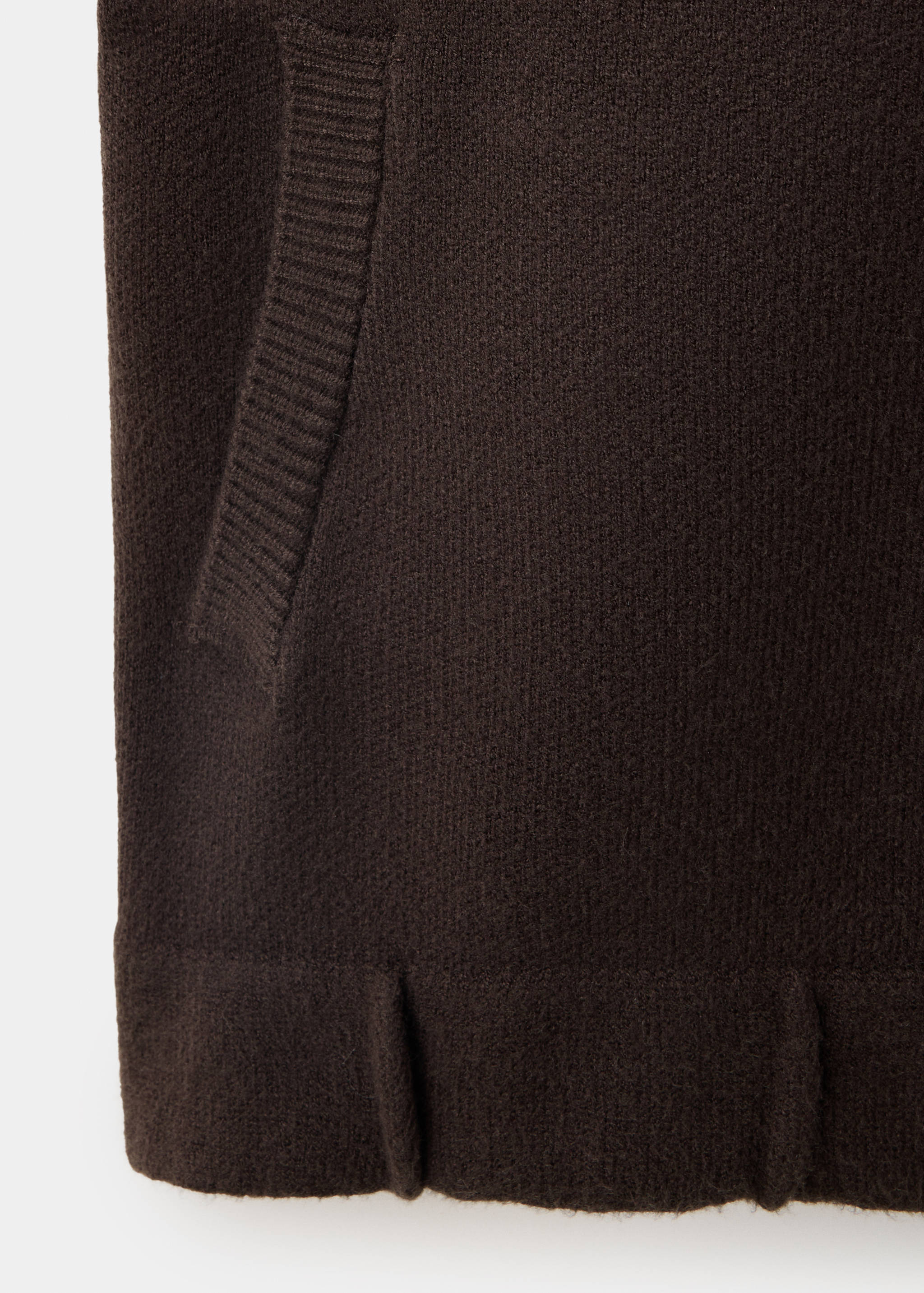 Detalle de chaqueta de punto marrón con bolsillo y dobladillo acanalado.