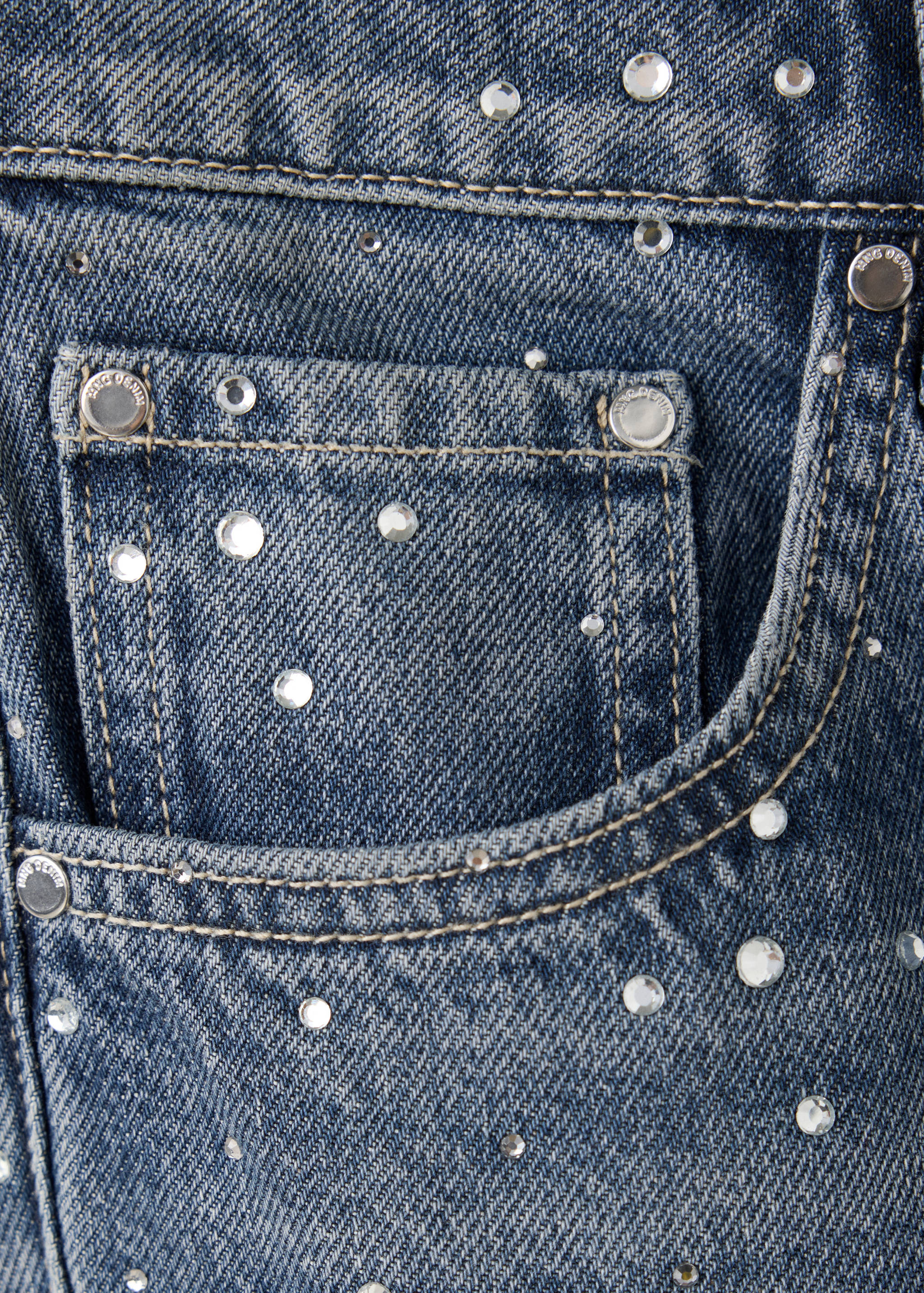 Close-up of blue denim trousers with scattered rhinestone embellishments.
