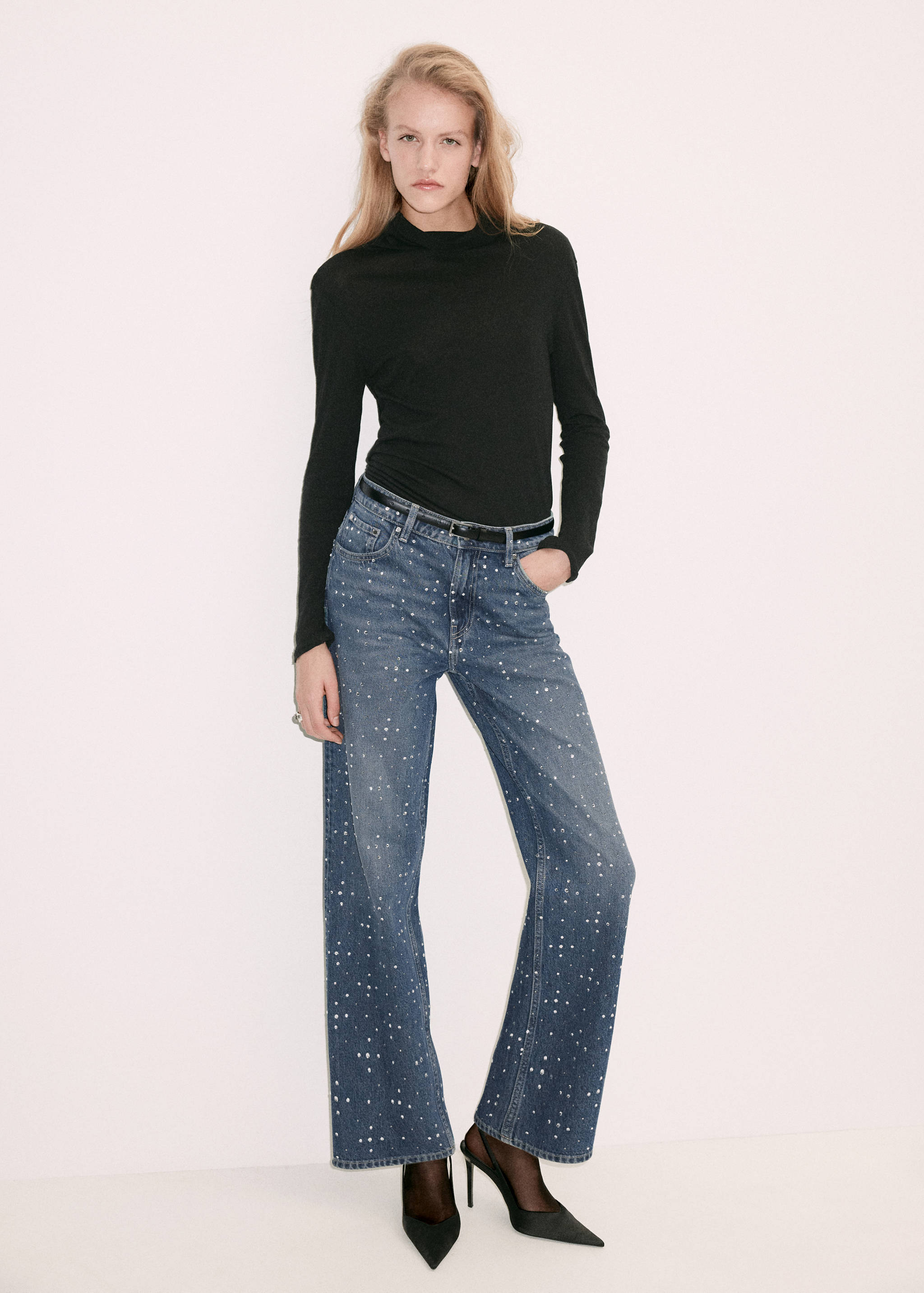 Blue embellished denim trousers worn with a black long-sleeve top.