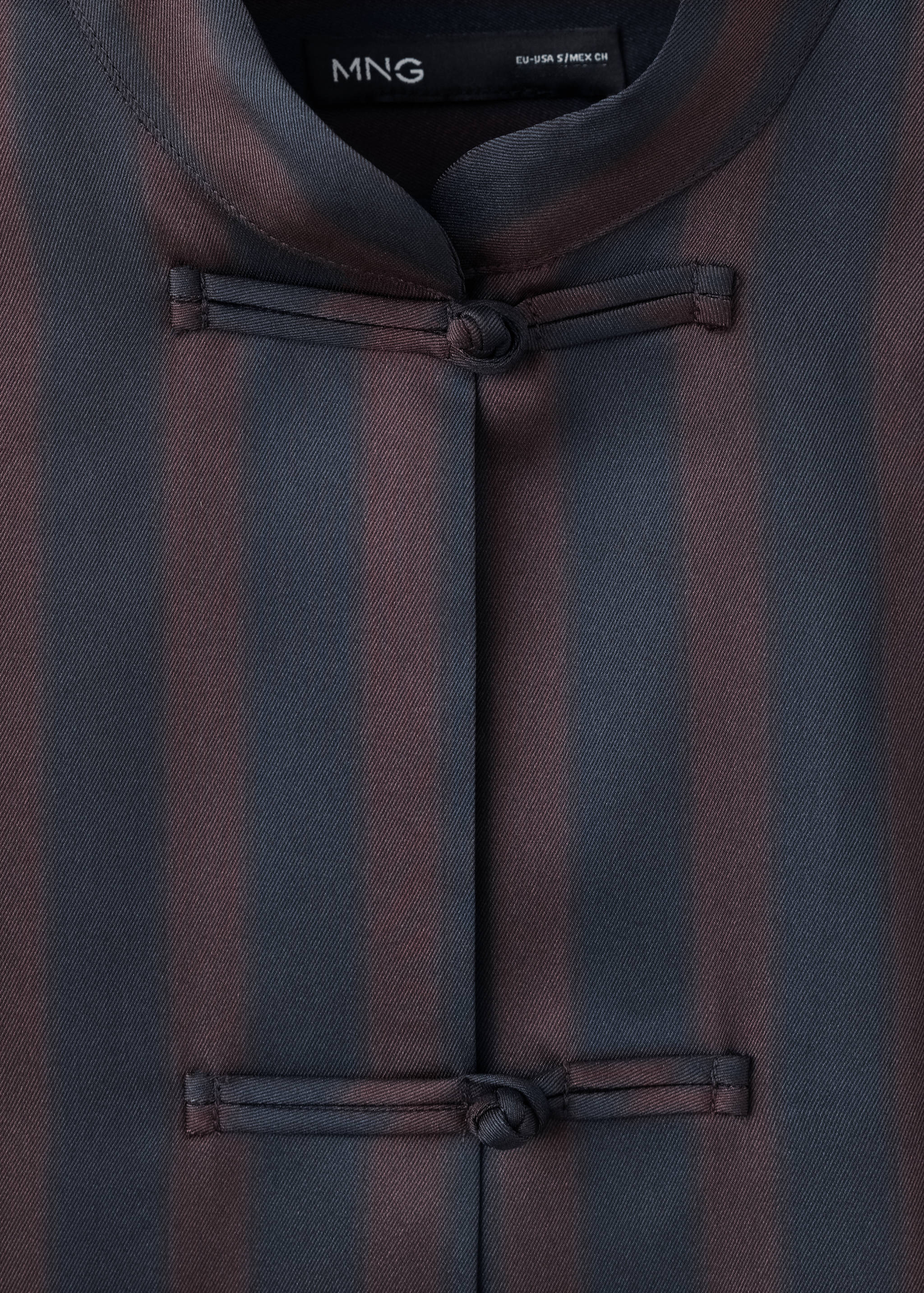 Close-up of a striped blouse with a mandarin collar and knotted closures.