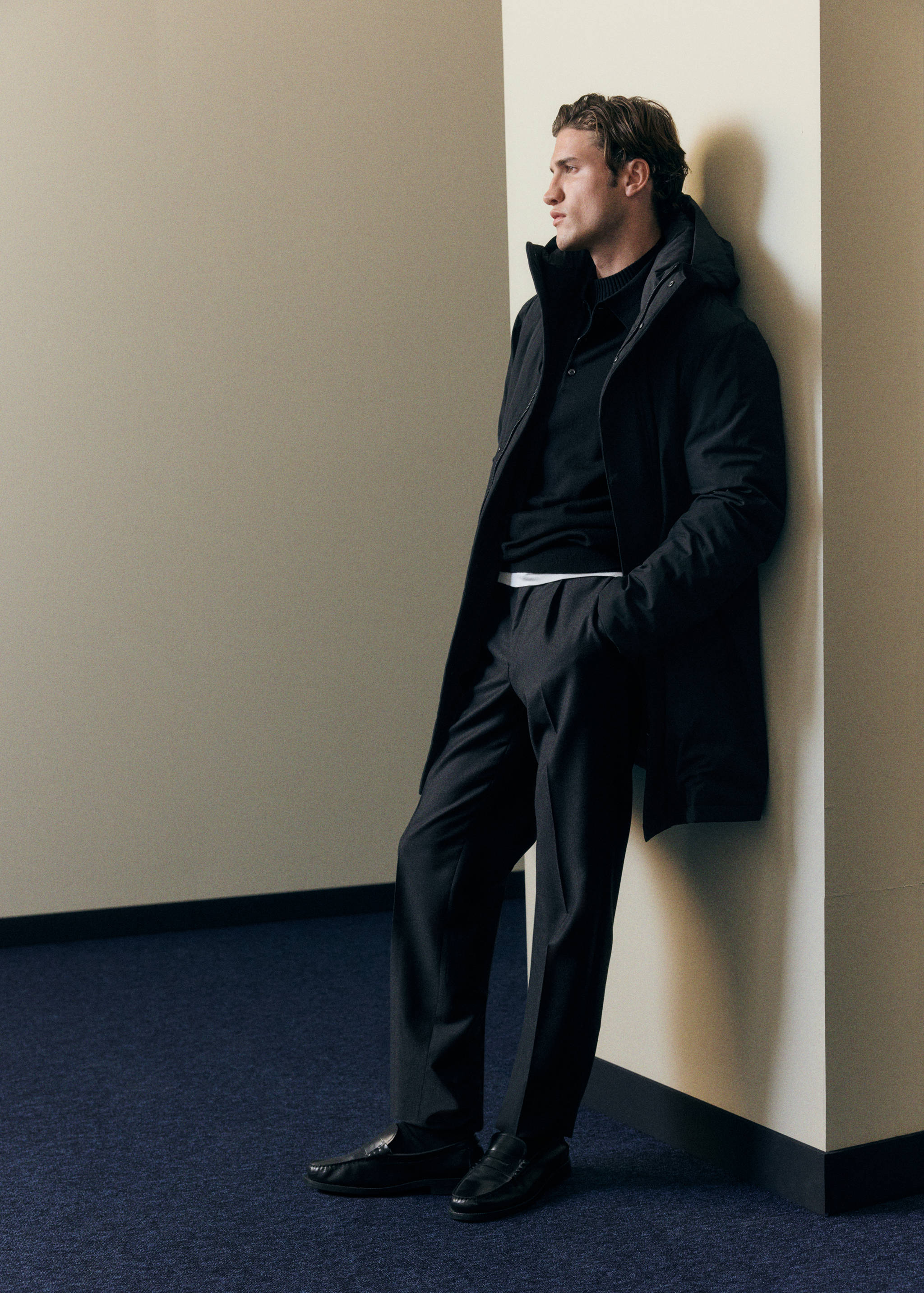 Black hooded parka with a high collar and front zip, worn over dark grey trousers.