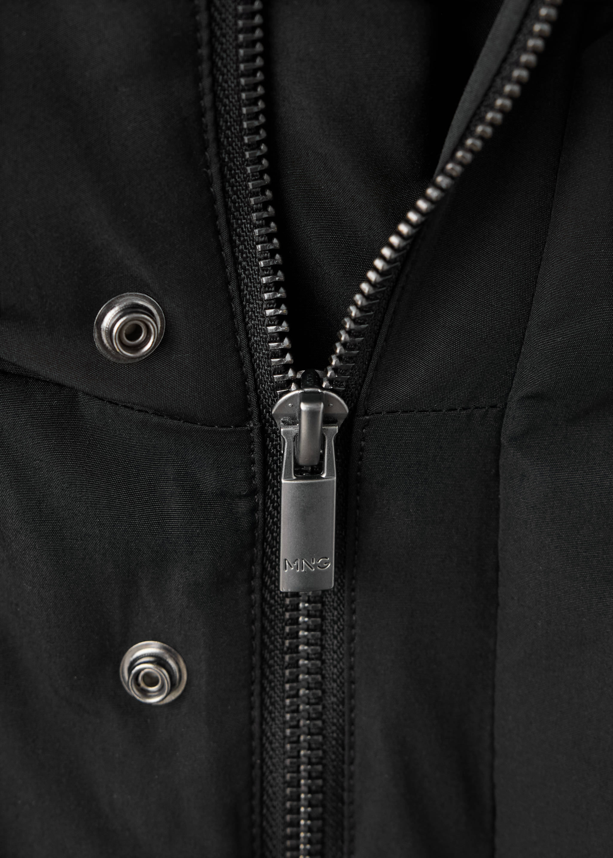 Close-up of a black parka featuring a zipped fastening and metal snap buttons.