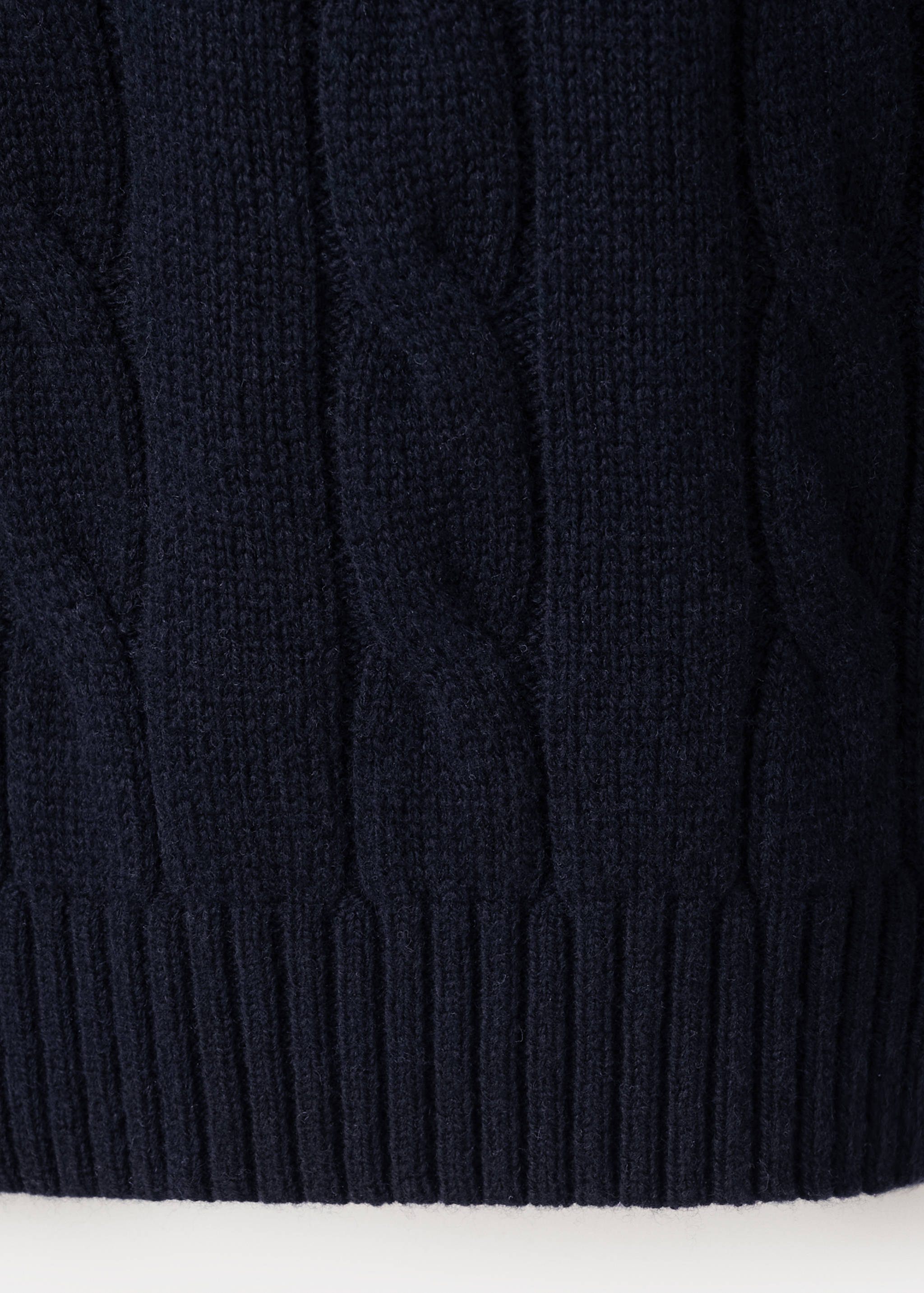 Close-up of the dark navy blue cable-knit fabric and ribbed hem of a polo.