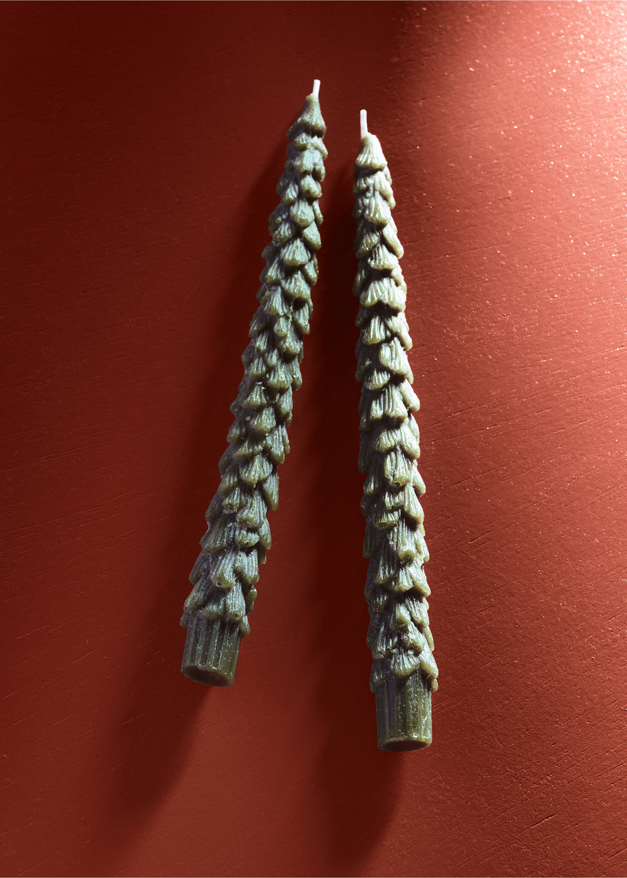 Two green pine tree-shaped candles on a red surface., Green. Ref: 37097889-00.