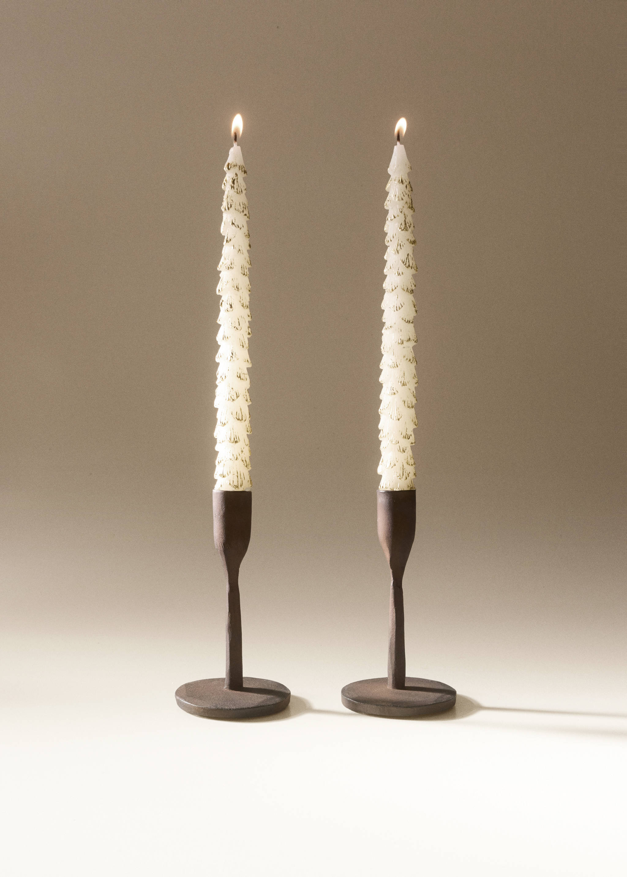 Two lit white tapered candles with gold speckled detailing in dark wooden holders.
