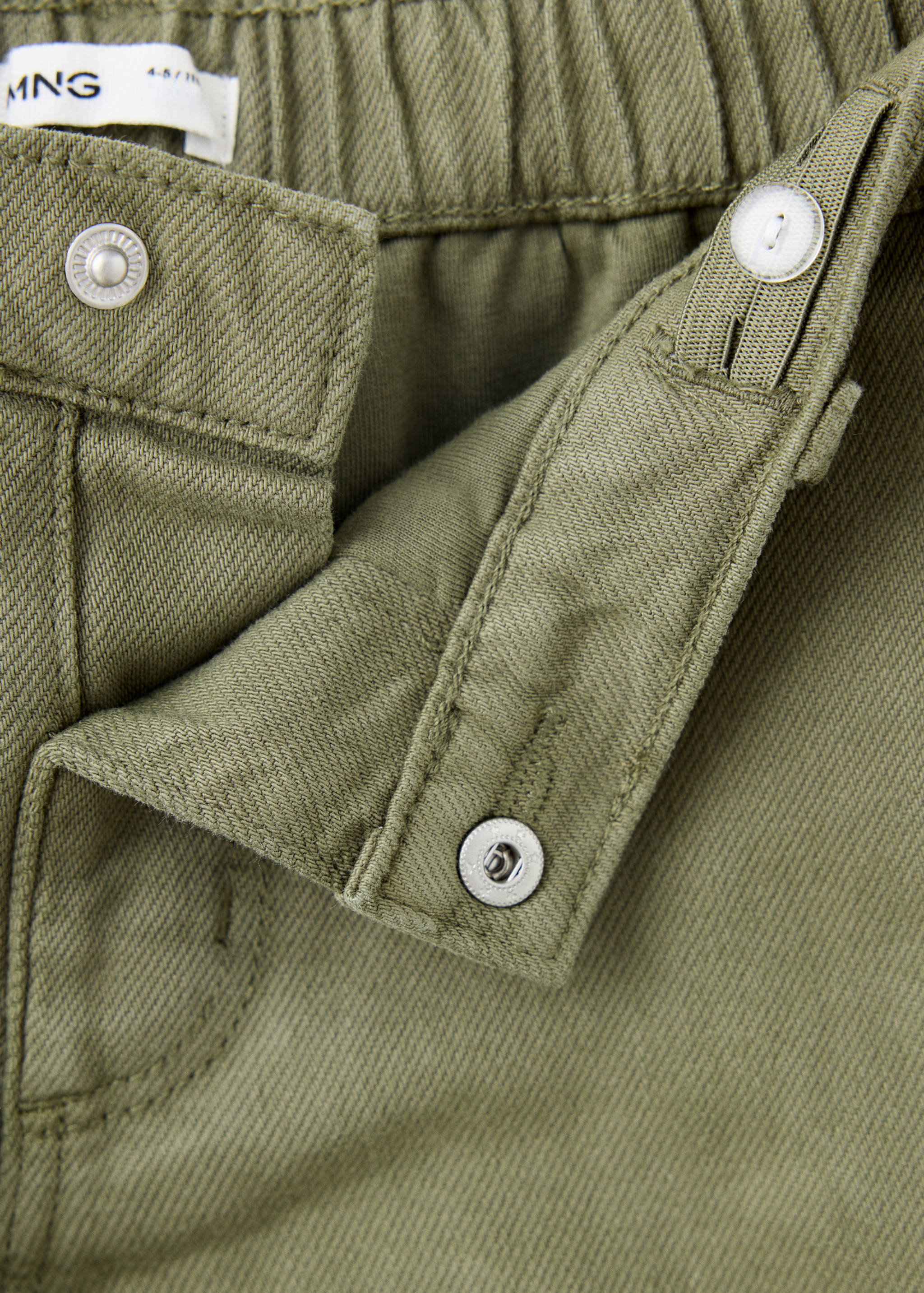 Close-up of green trousers showcasing the waistband and snap-button fastening detail.