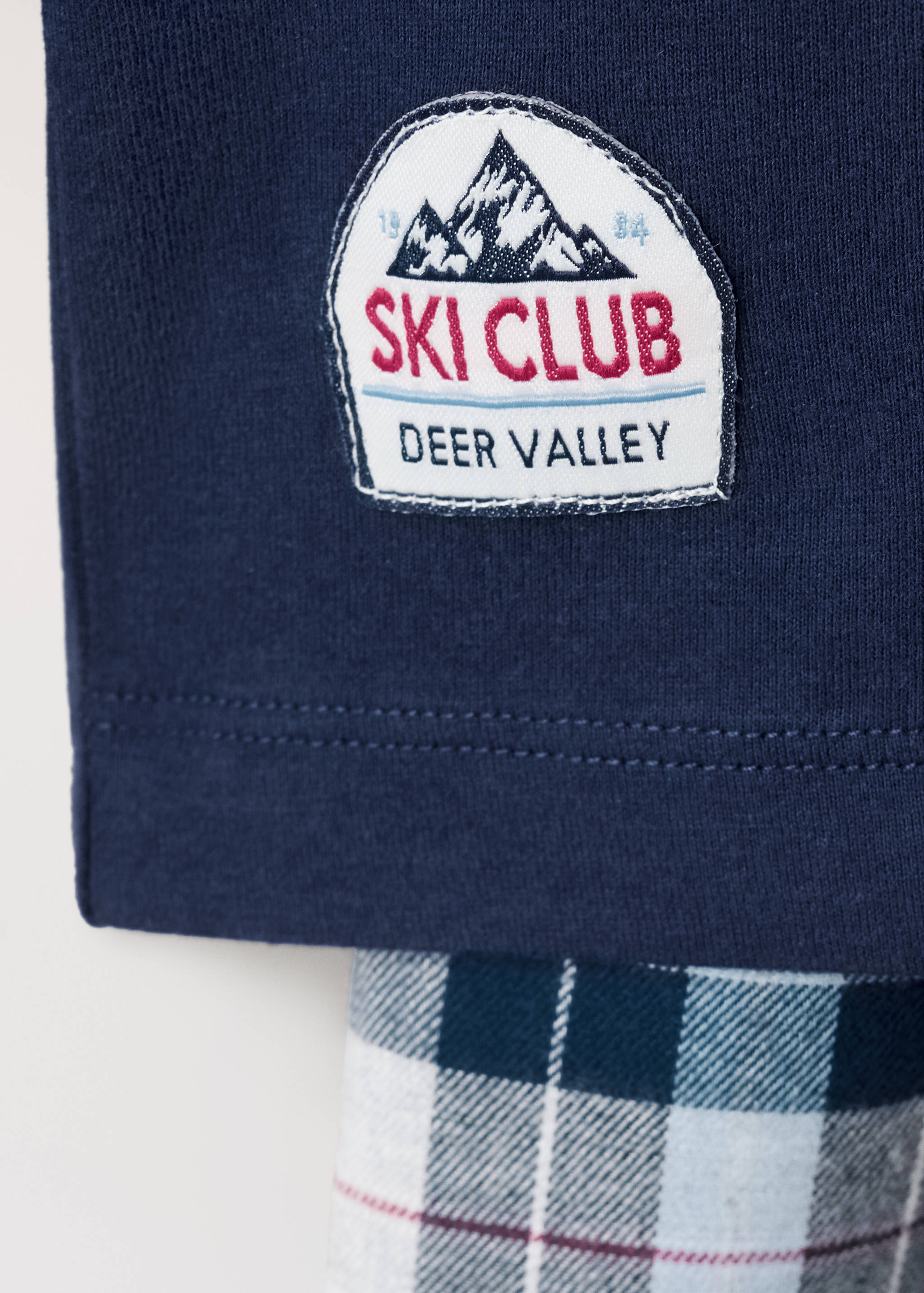 Close-up of a navy pyjama top with a Ski Club Deer Valley patch and plaid trousers.