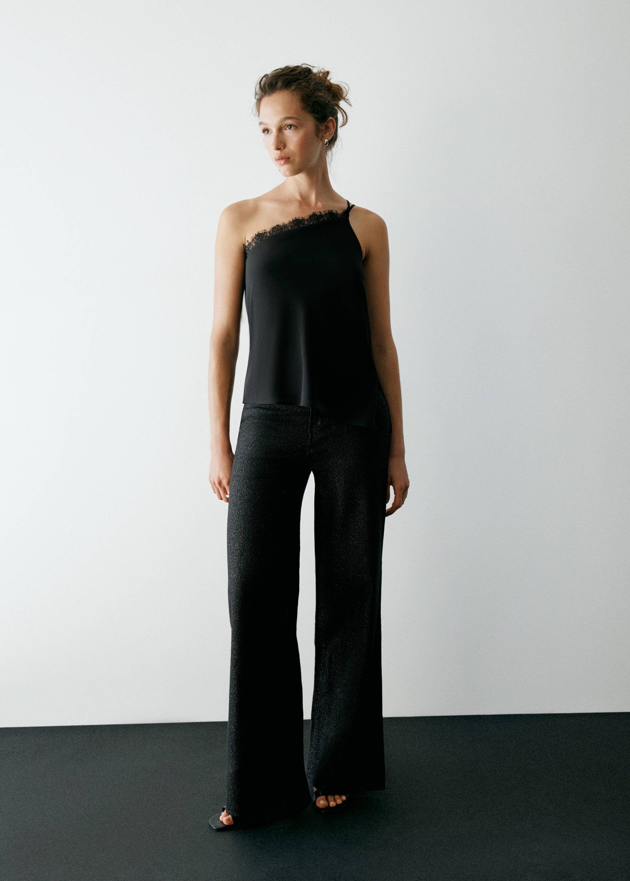 Pantalones anchos metalizados negros combinados con un top asimétrico de un solo hombro.