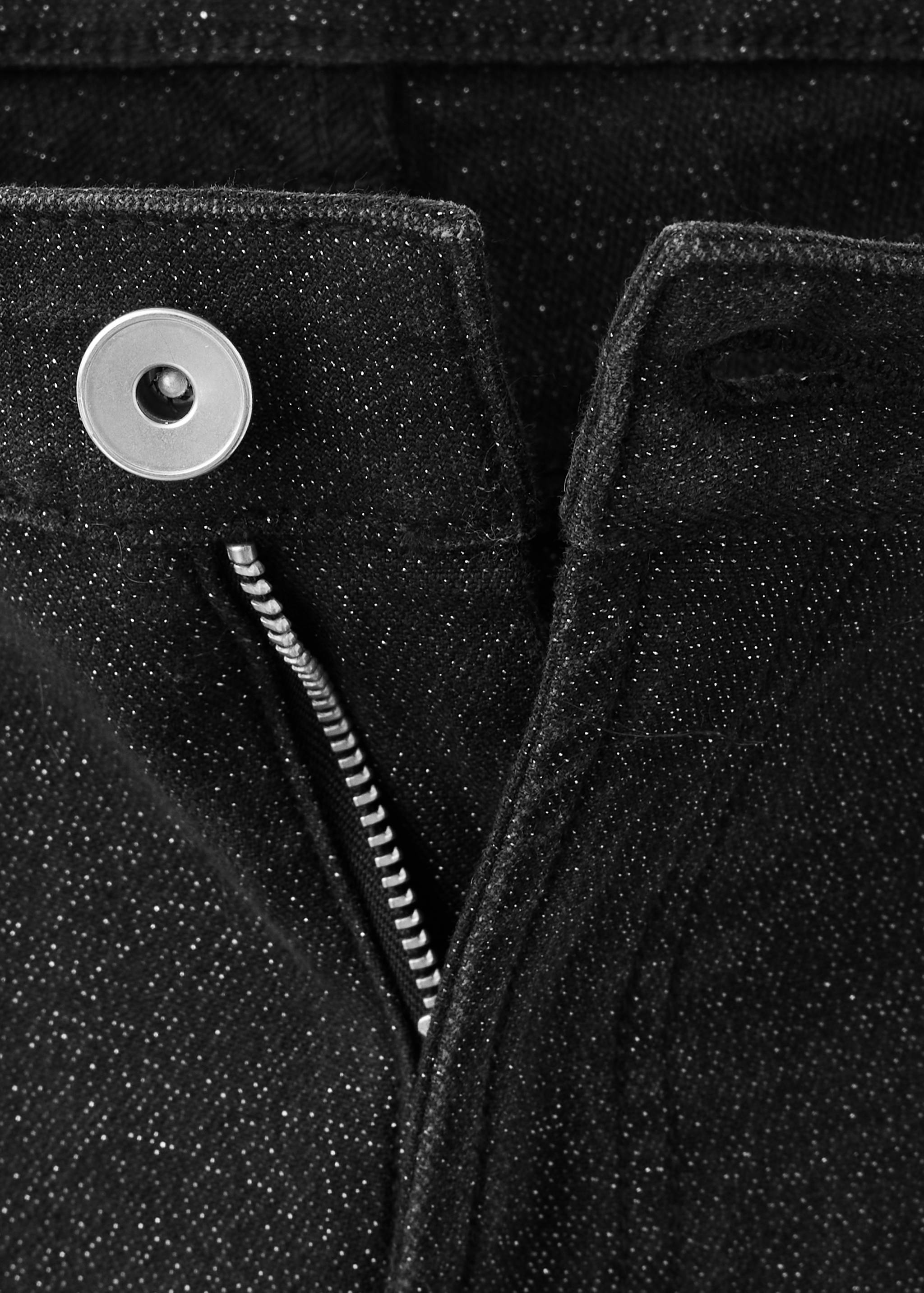 Primer plano de pantalones vaqueros negros con brillo y detalle de botón y cremallera.