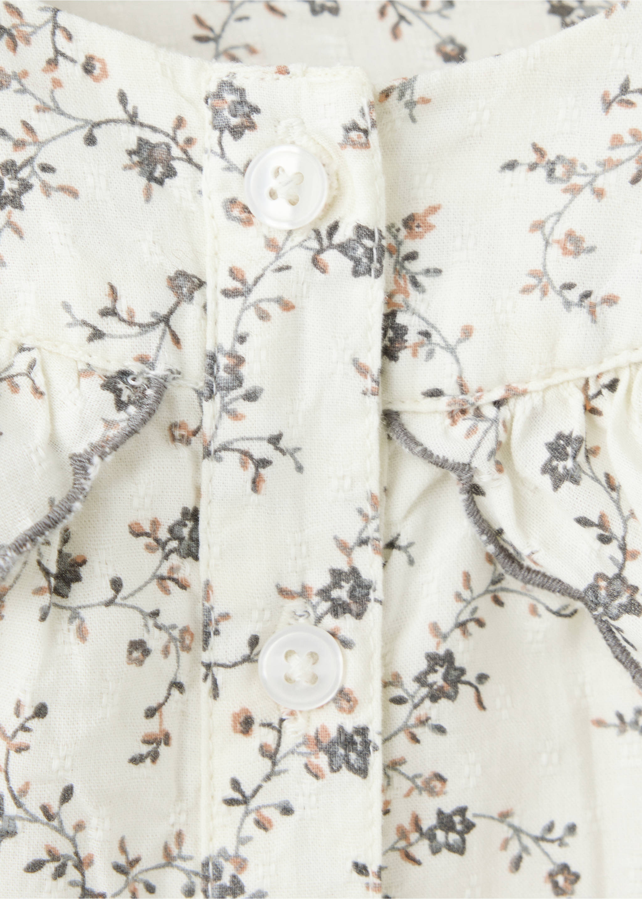 Close-up of a floral print children's dress with ruffled shoulders and white buttons., Ecru. Ref: 37097925-00.