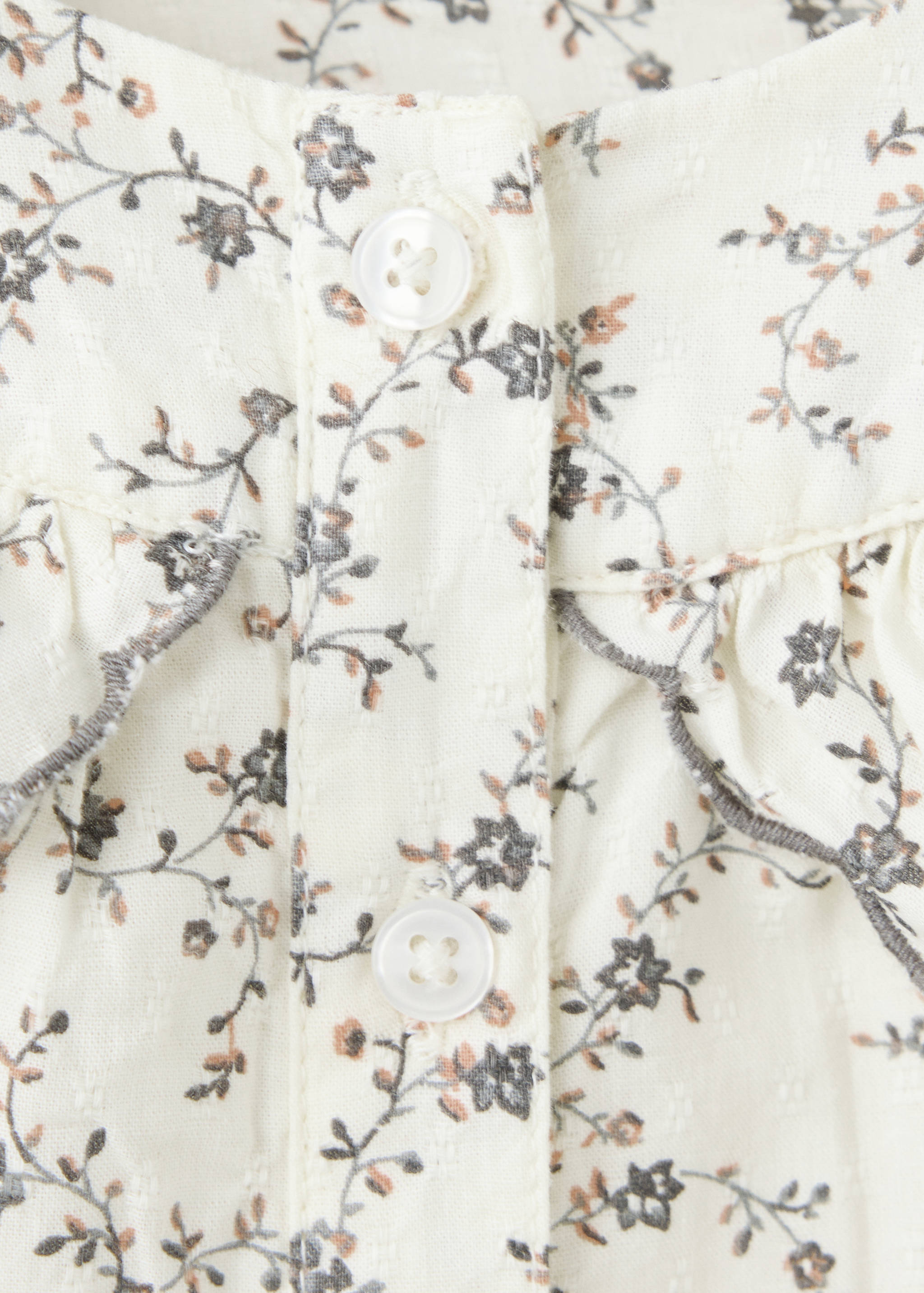 Close-up of a floral print children's dress with ruffled shoulders and white buttons.