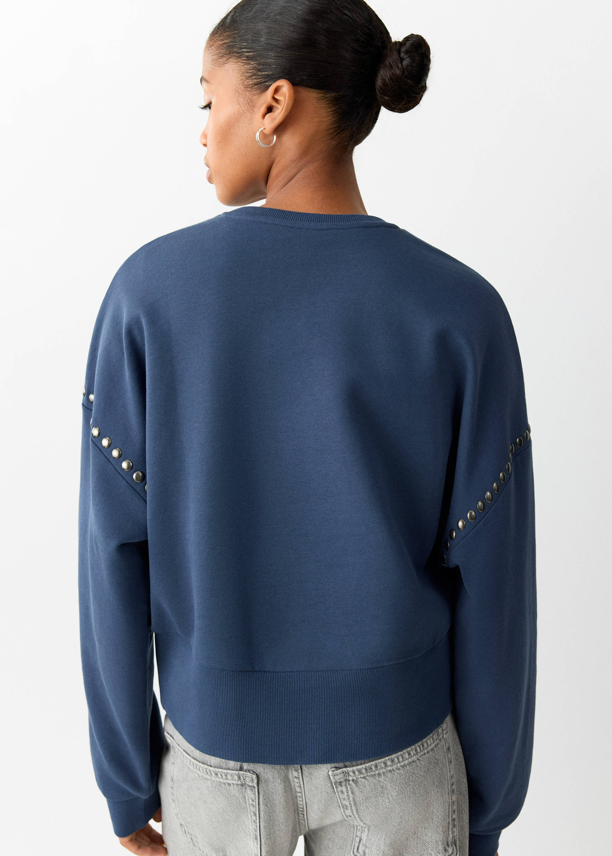 Sudadera azul oscuro con detalles de tachuelas metálicas en las mangas, vista posterior.