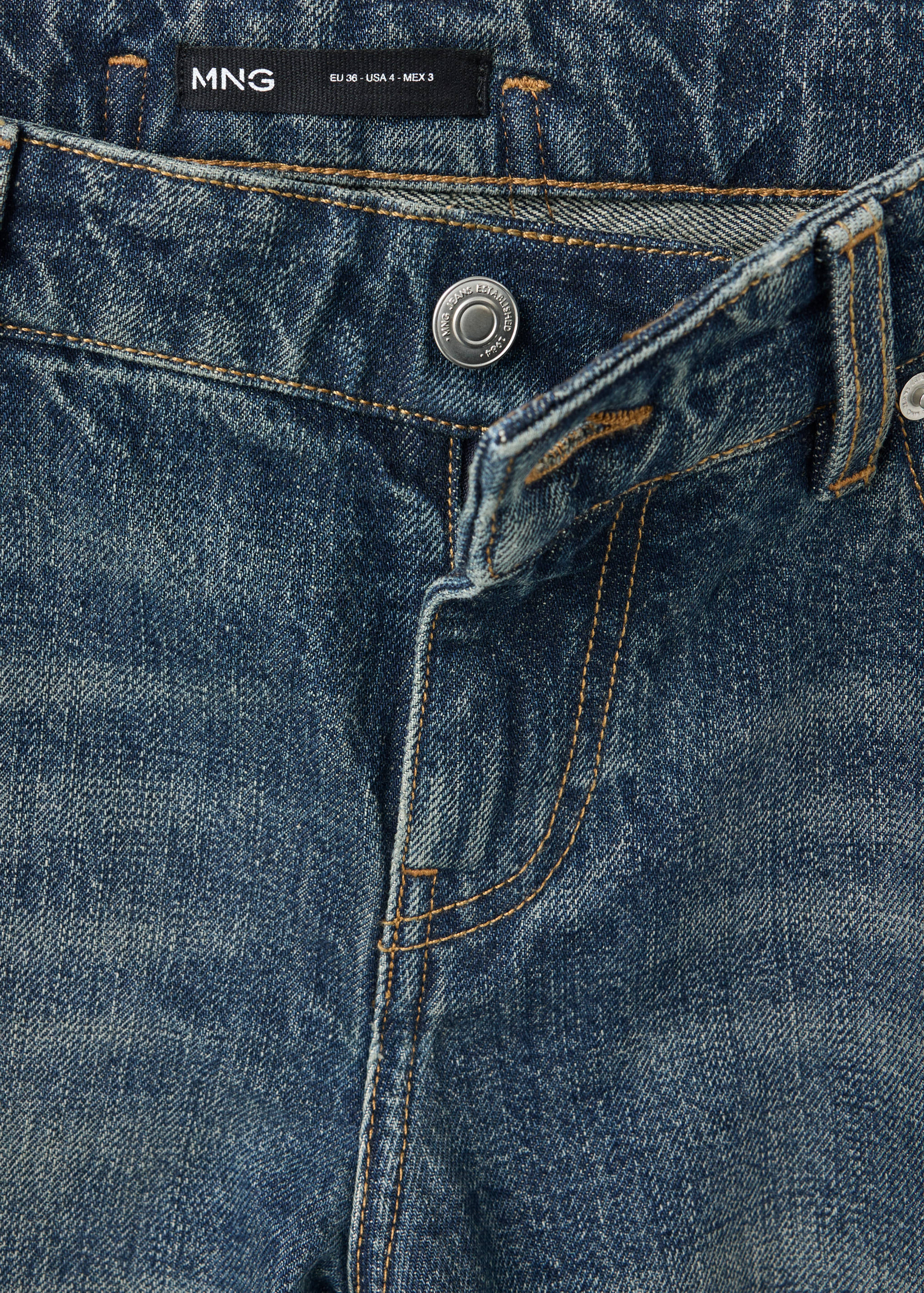 Close-up of blue denim trousers showing the waistband, zip fly, and button.