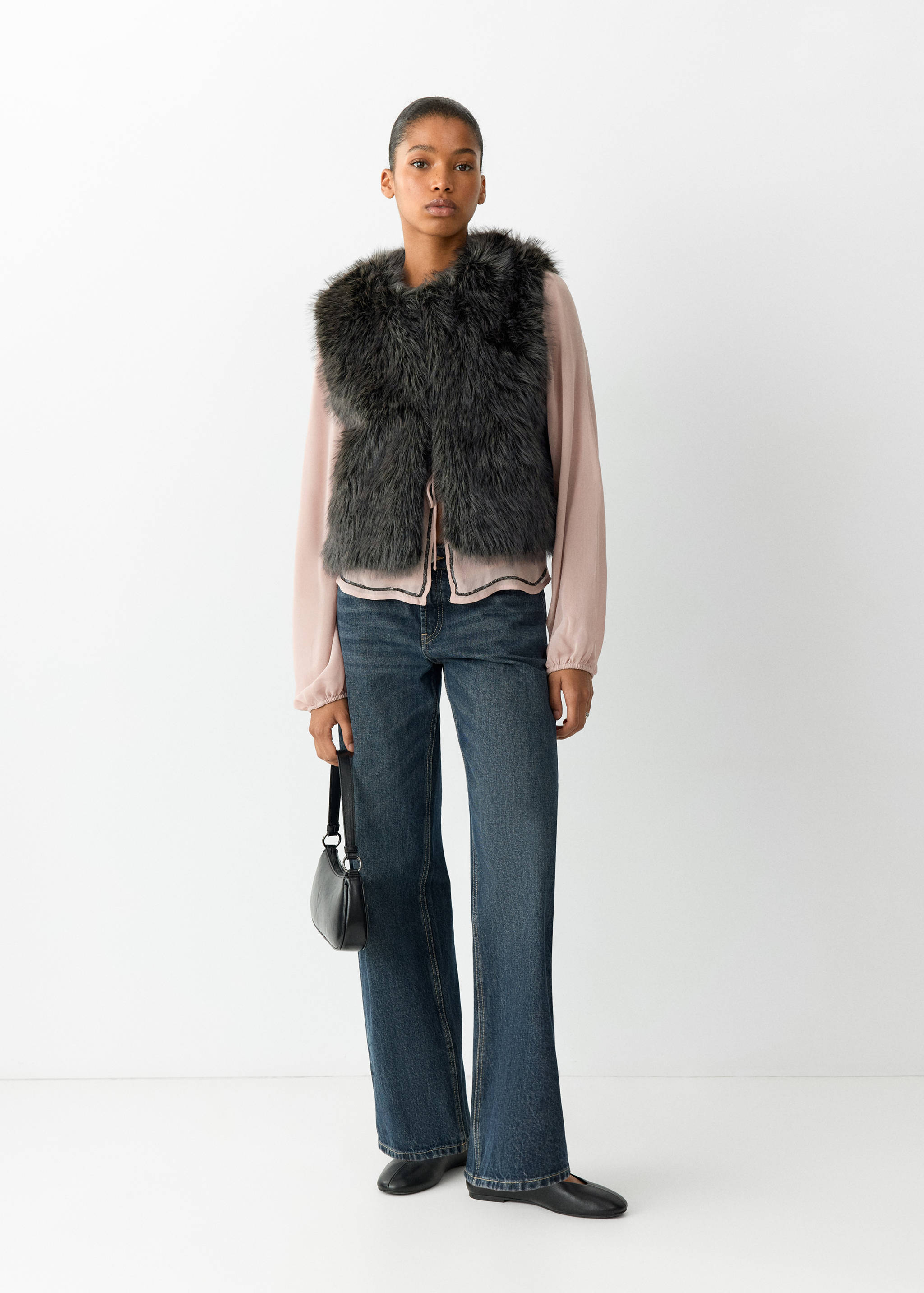 Dark grey faux-fur vest worn over a pink blouse and blue trousers.