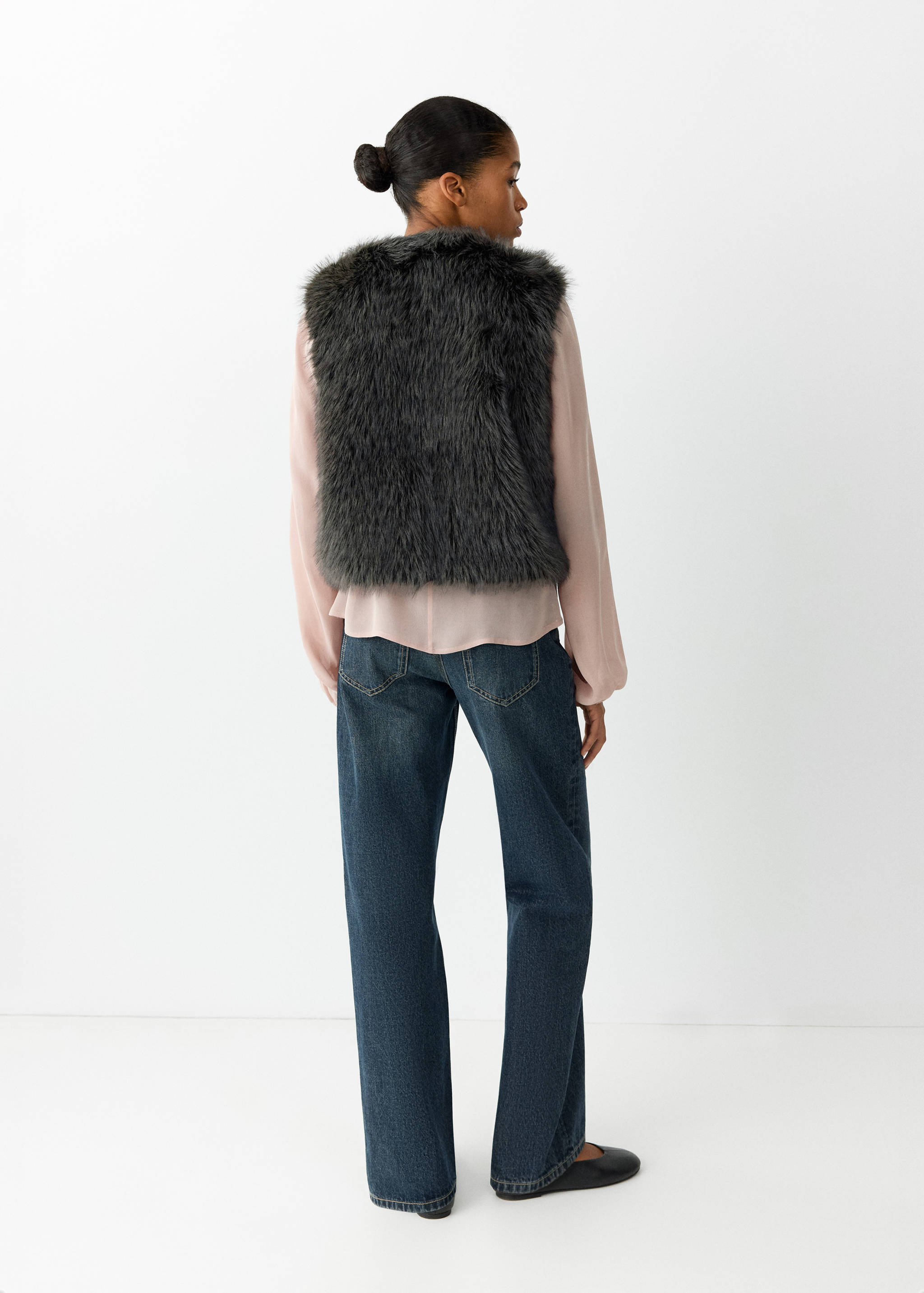 Dark grey sleeveless faux-fur vest, seen from the back on a model.