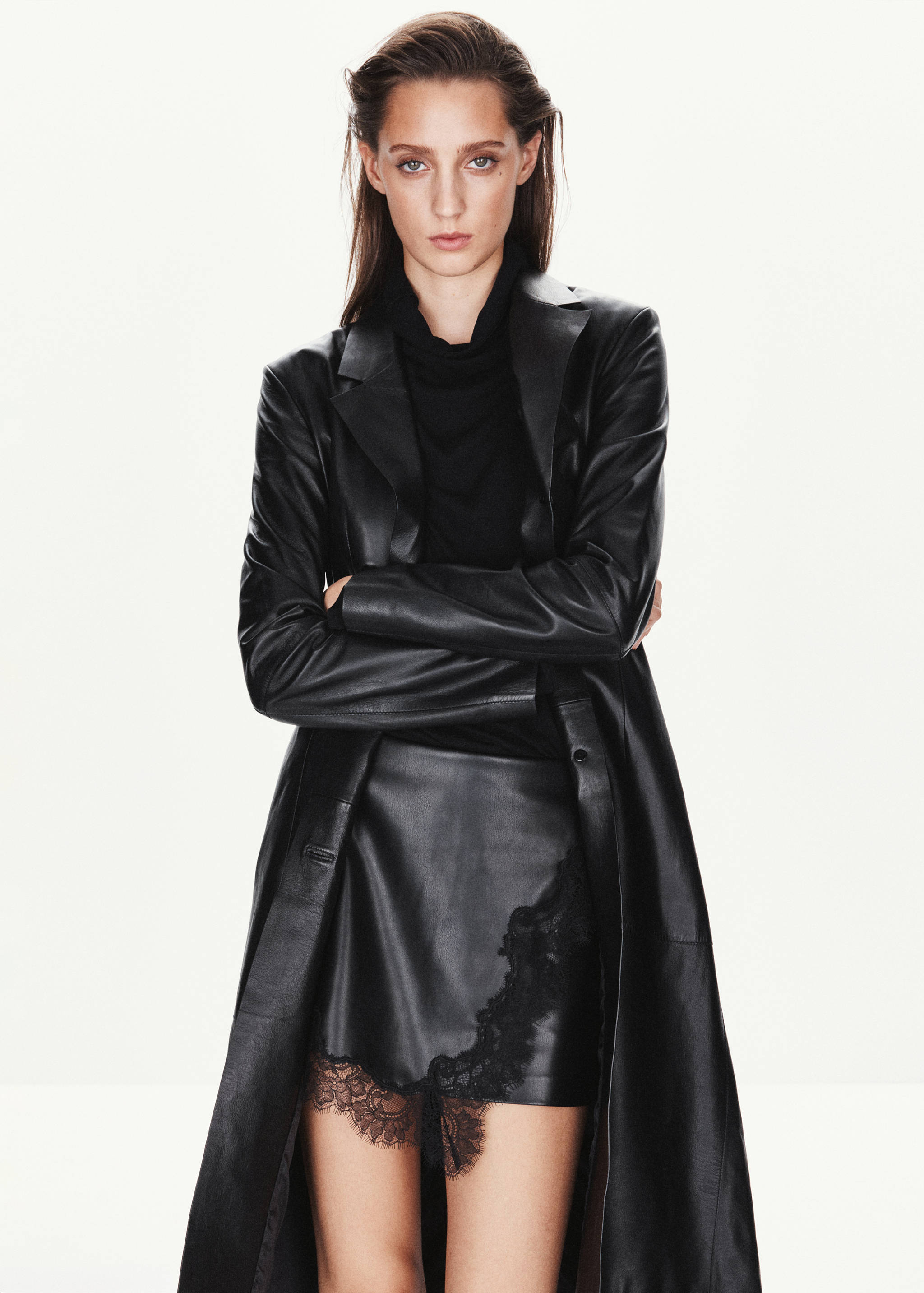 Black mini skirt with asymmetric lace trim, worn with a black top and long faux-leather coat.