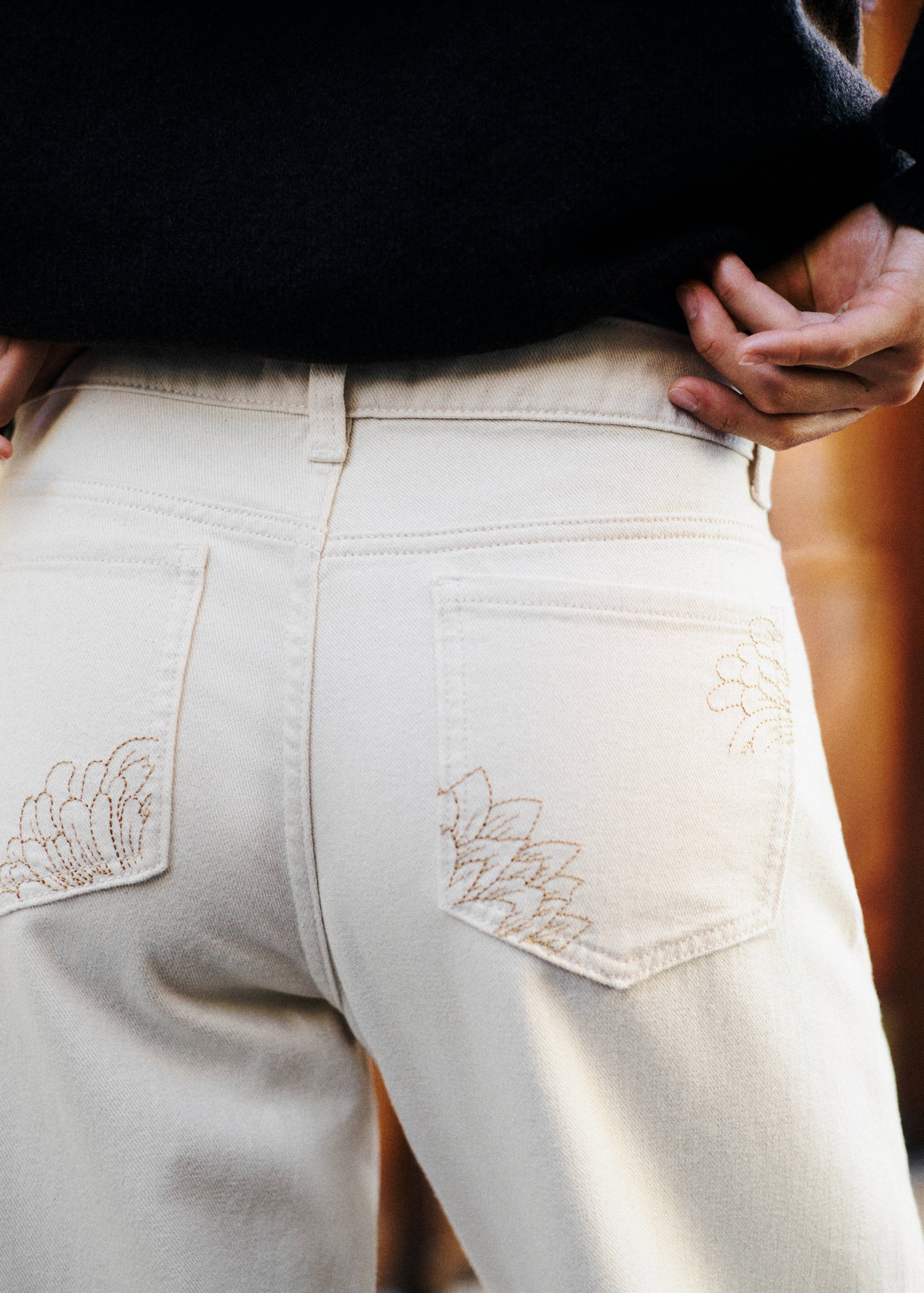 Back view of light beige trousers with embroidered pocket details.