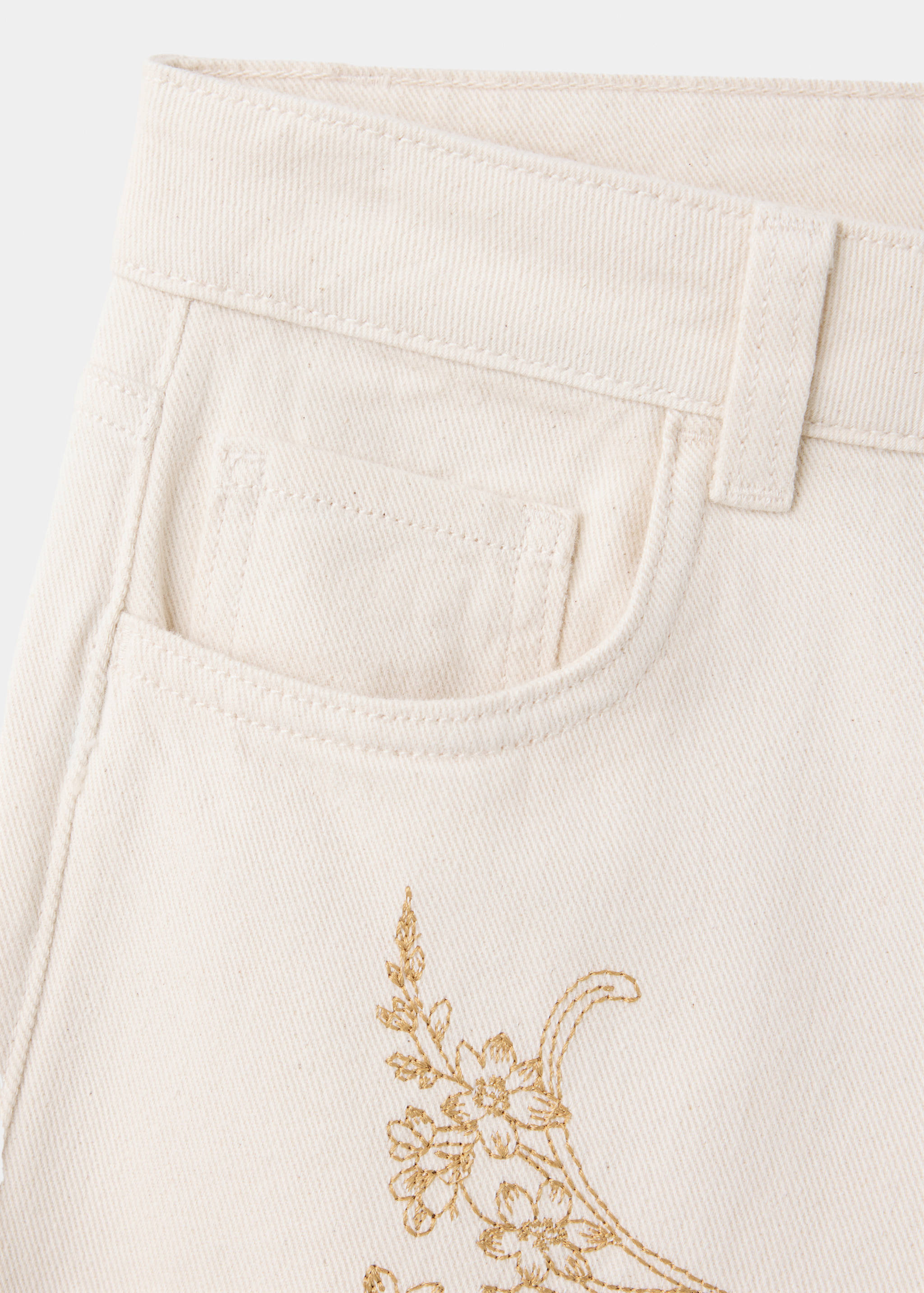 Close-up of off-white denim trousers with gold floral embroidery.