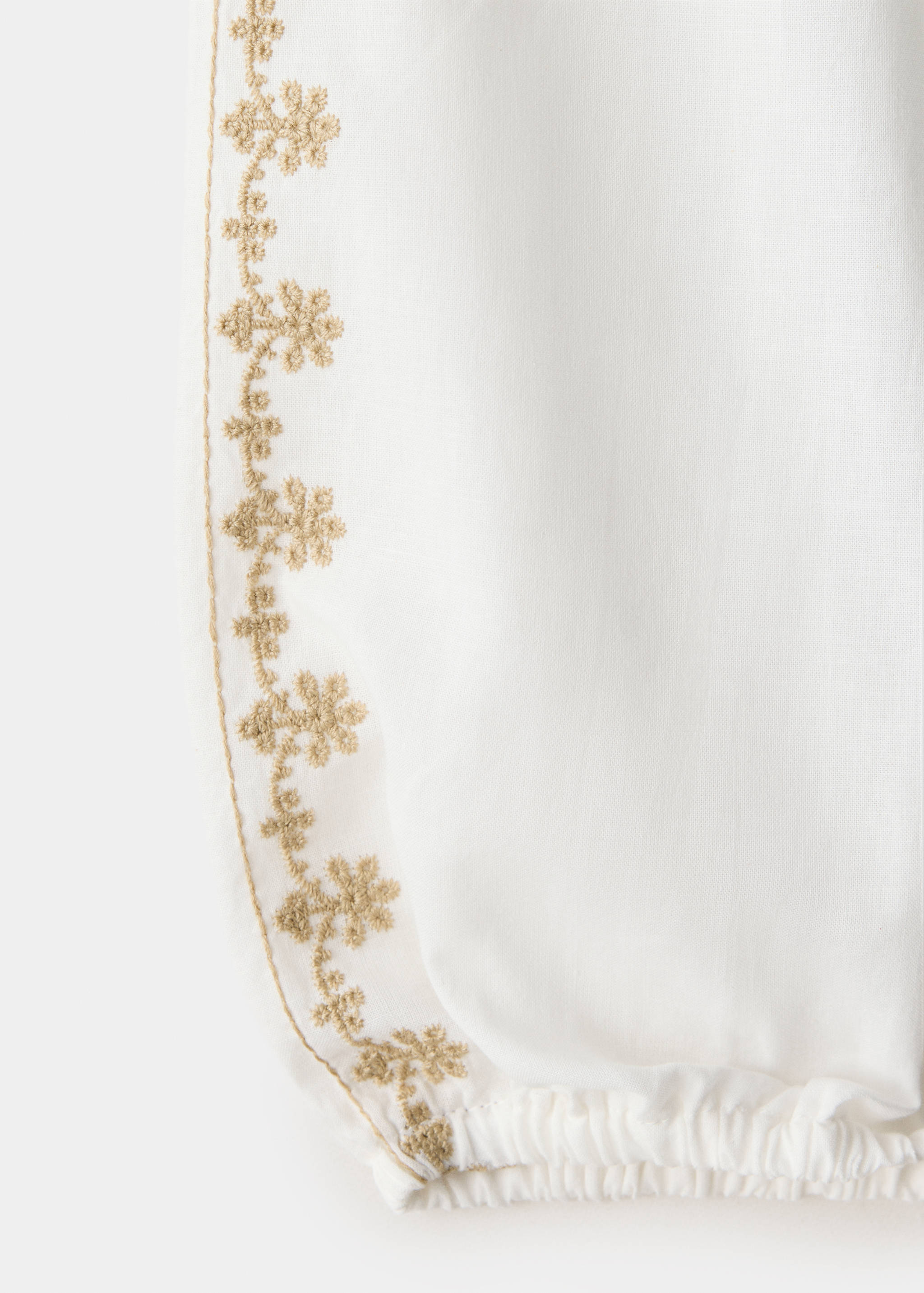 Close-up of a white shirt with gold floral embroidery detail.
