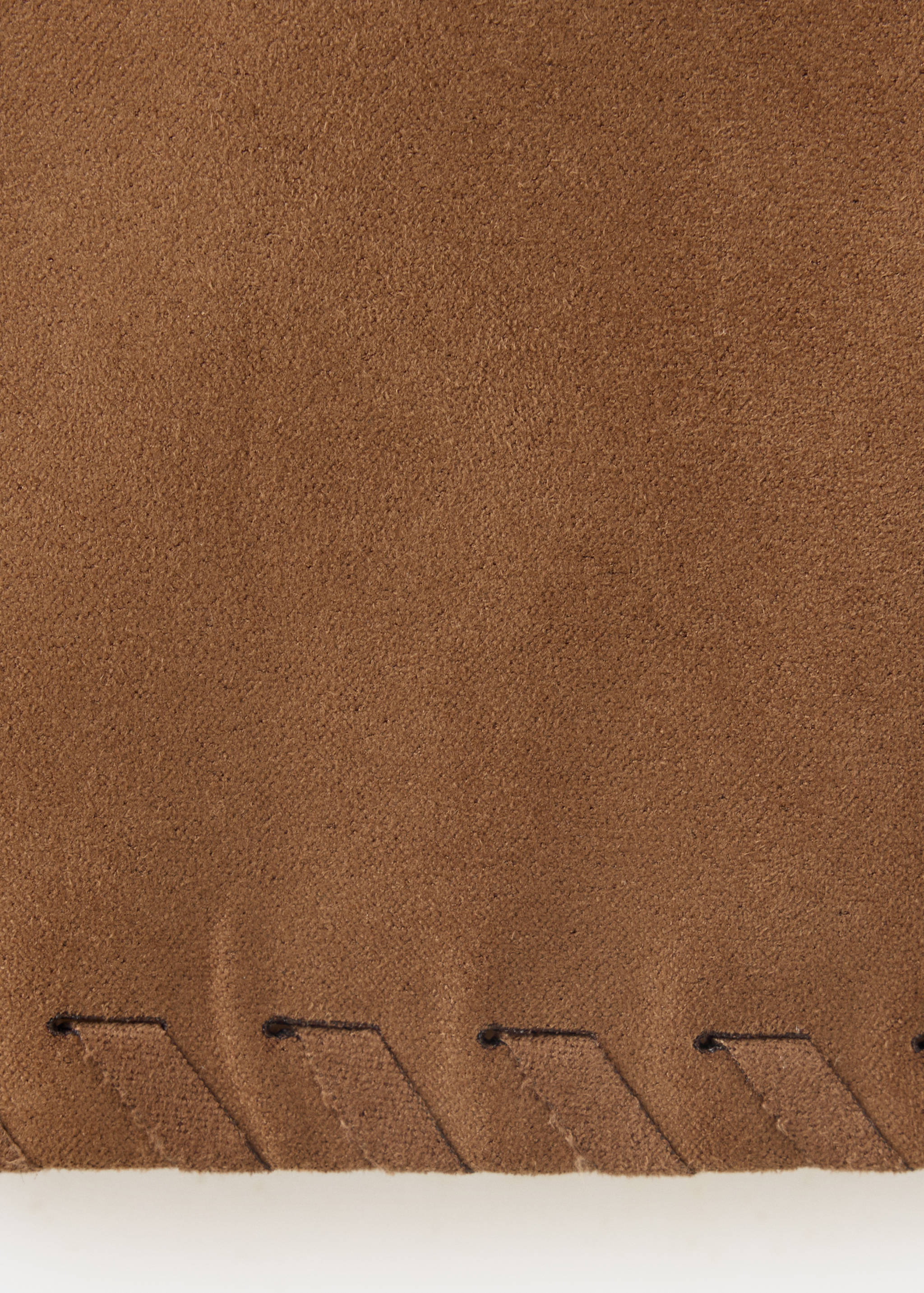 Brown skirt fabric detail showing suede-like texture and whipstitch hem.