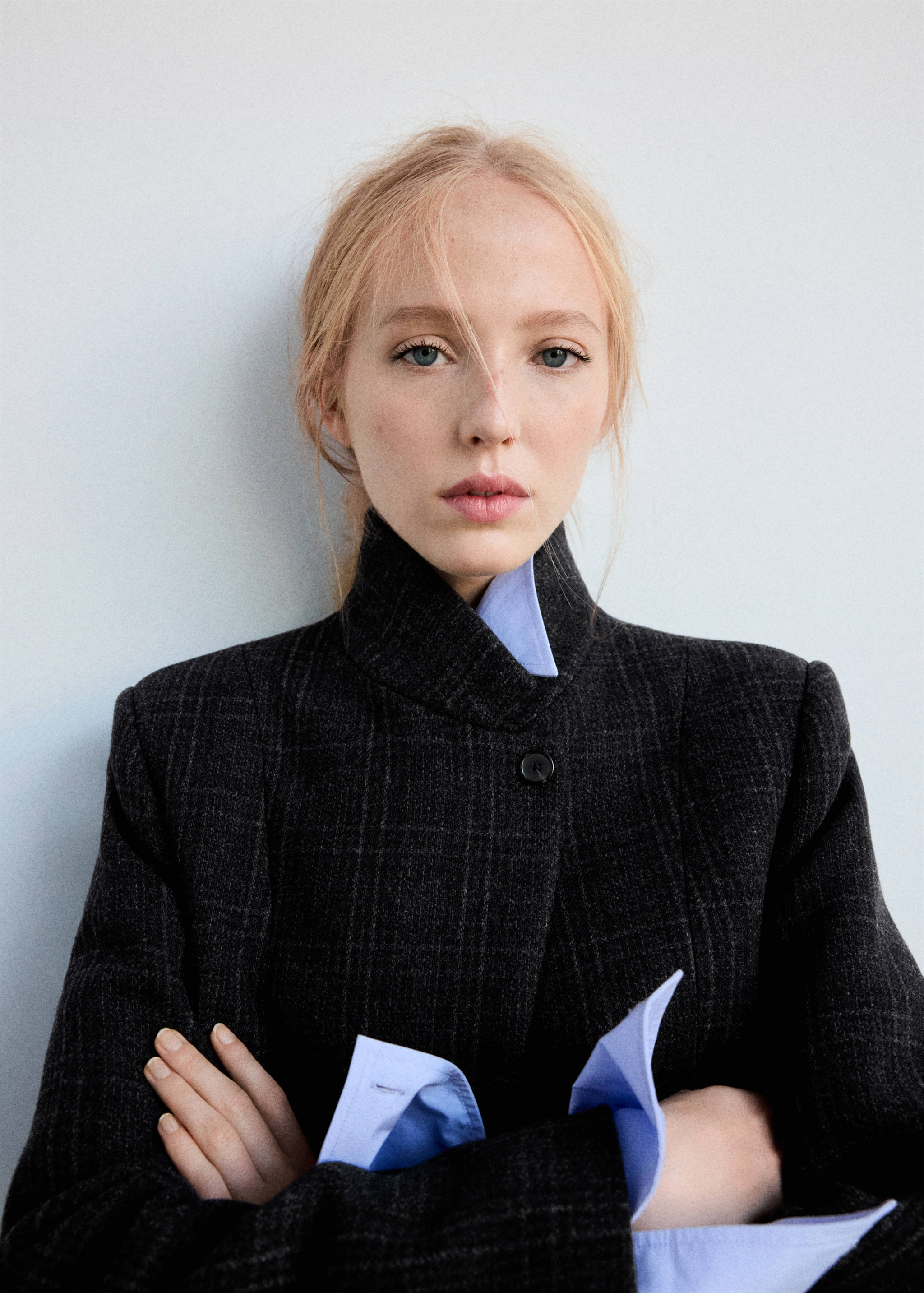 Close-up of a dark grey plaid coat with a high collar, layered with a light blue shirt.