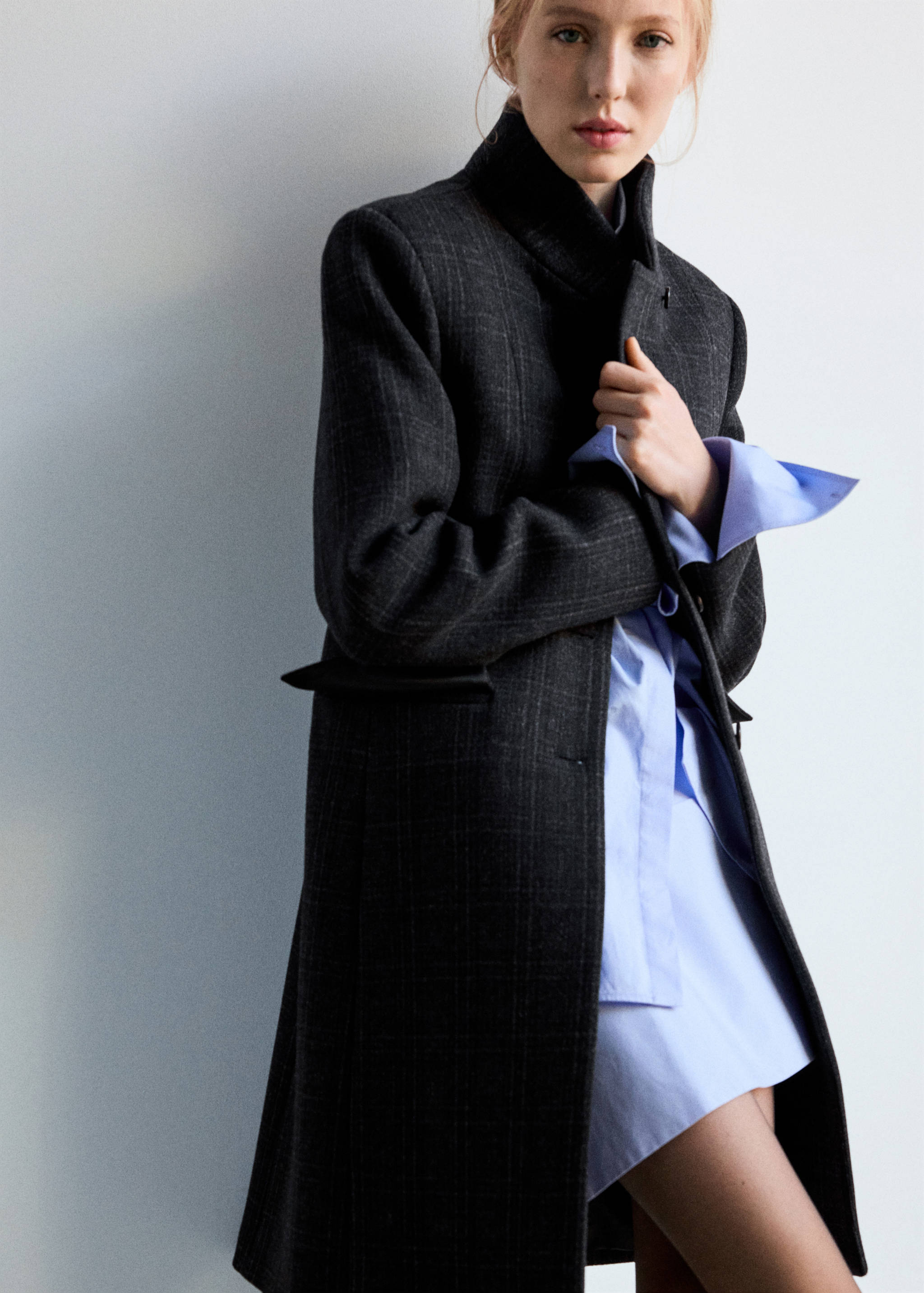Dark grey plaid coat with a high collar worn over a light blue shirt.