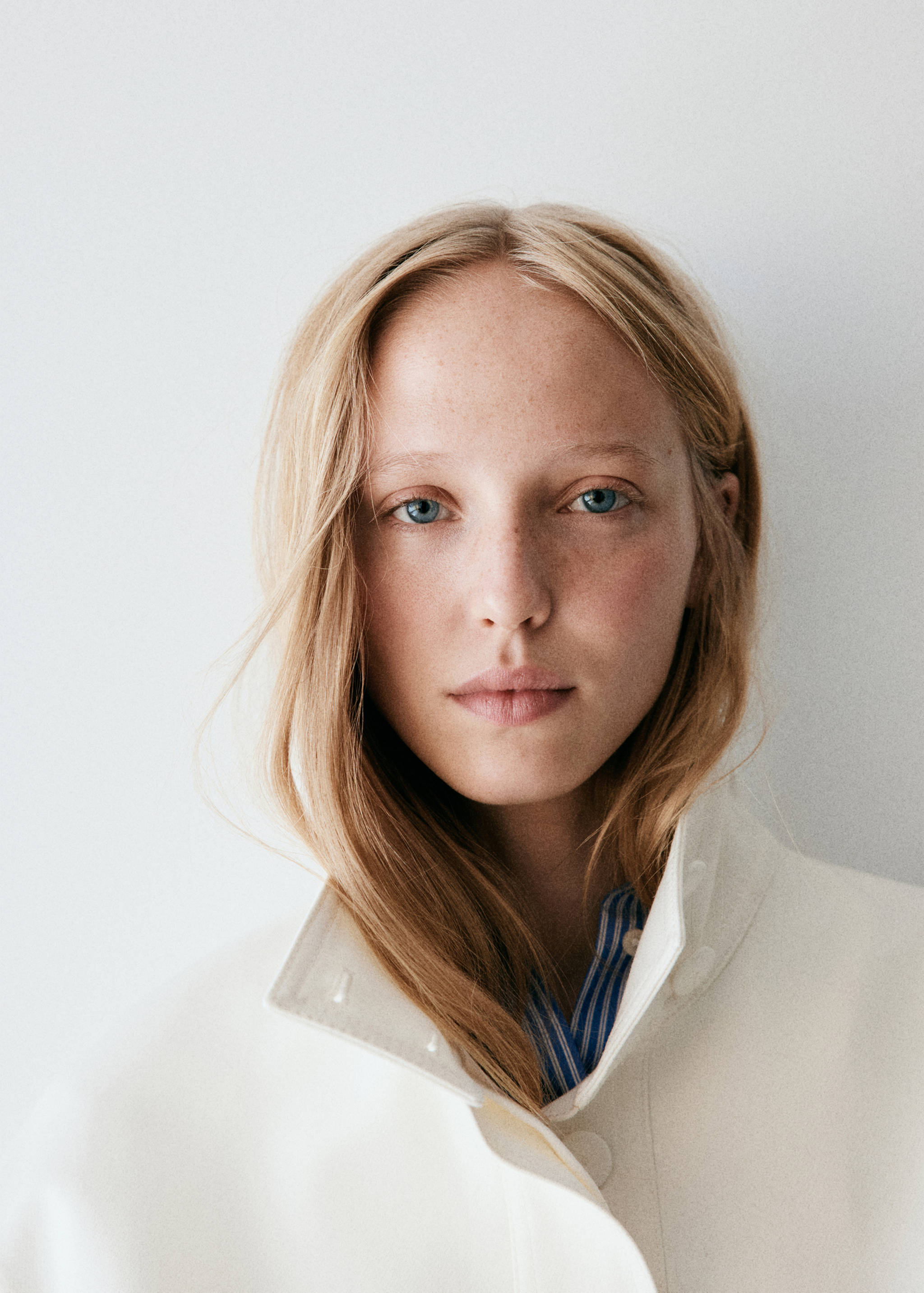 Close-up of a white jacket with a high collar worn over a striped shirt.