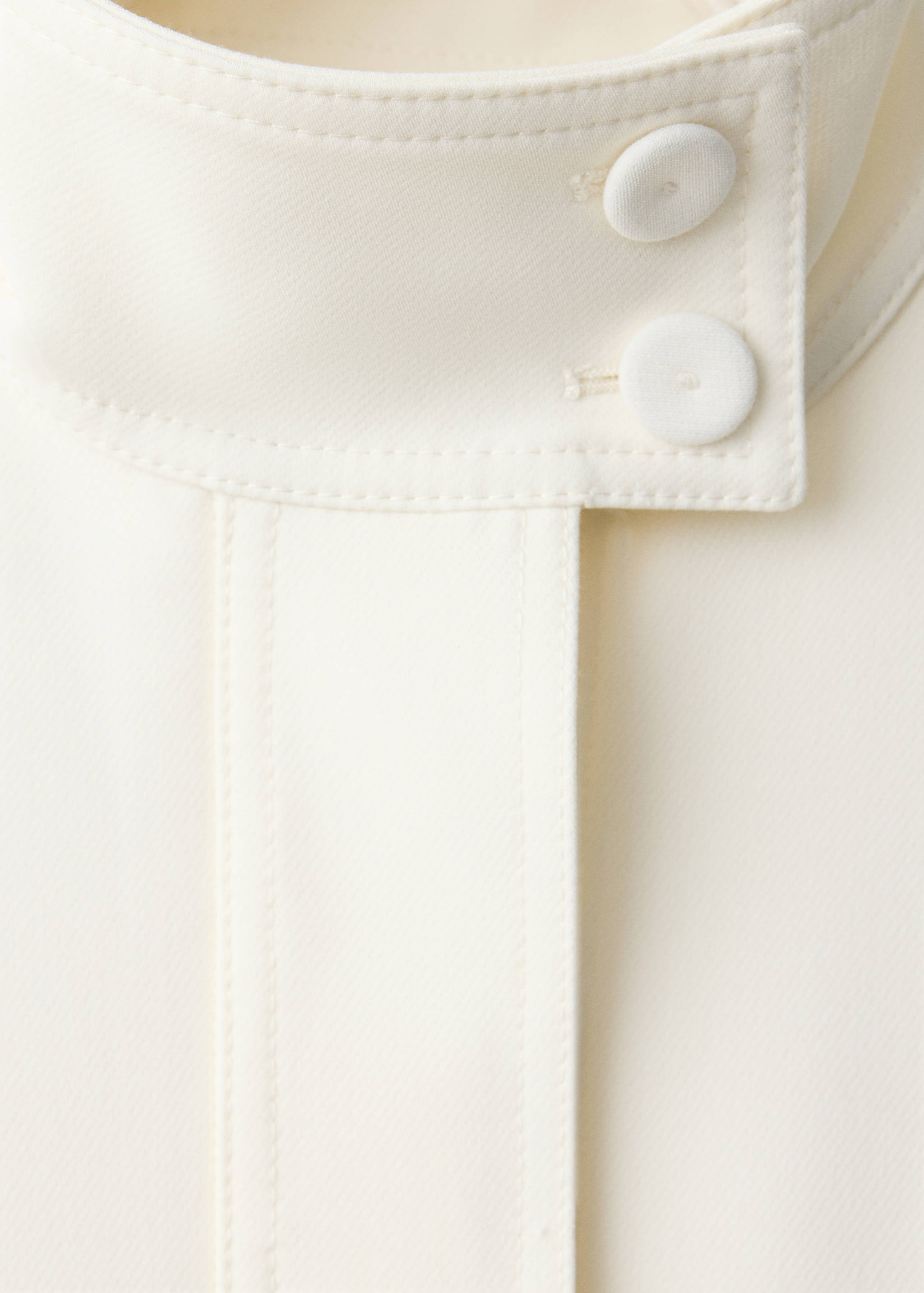 Cream jacket high collar detail with two fabric-covered buttons.