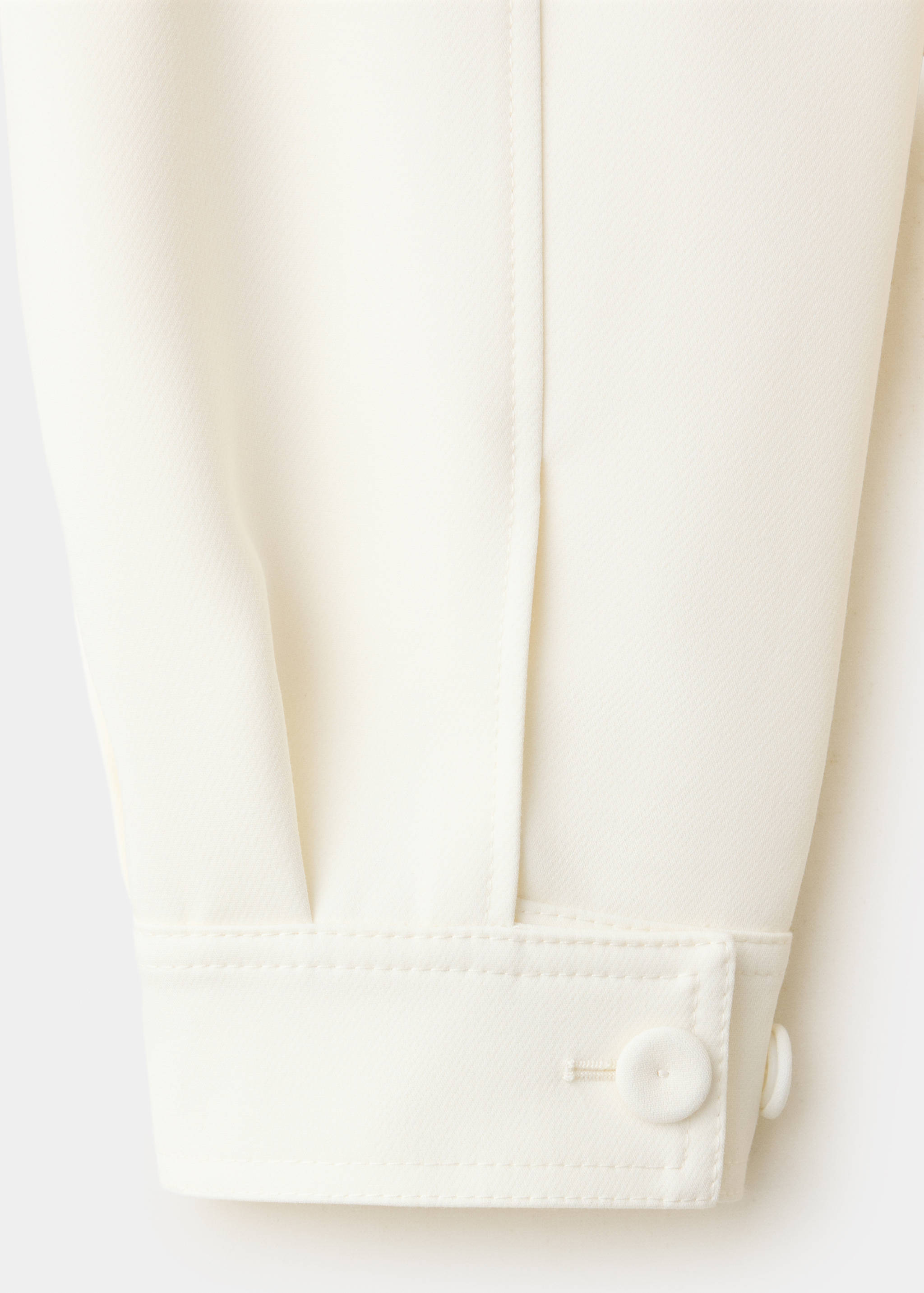 Close-up of off-white jacket sleeve with buttoned cuff.