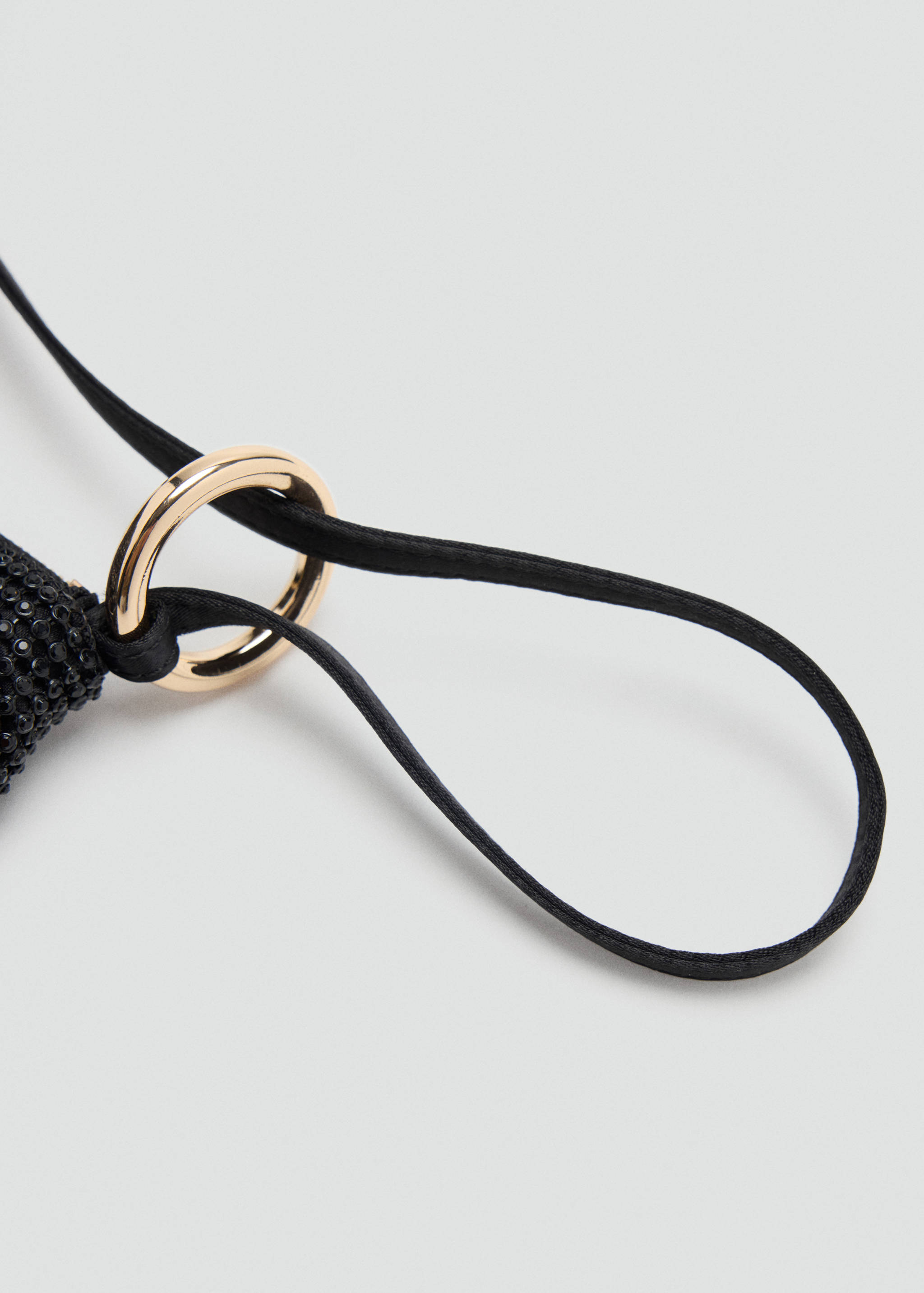 Close-up of a black handbag strap and gold-tone metal ring detail.
