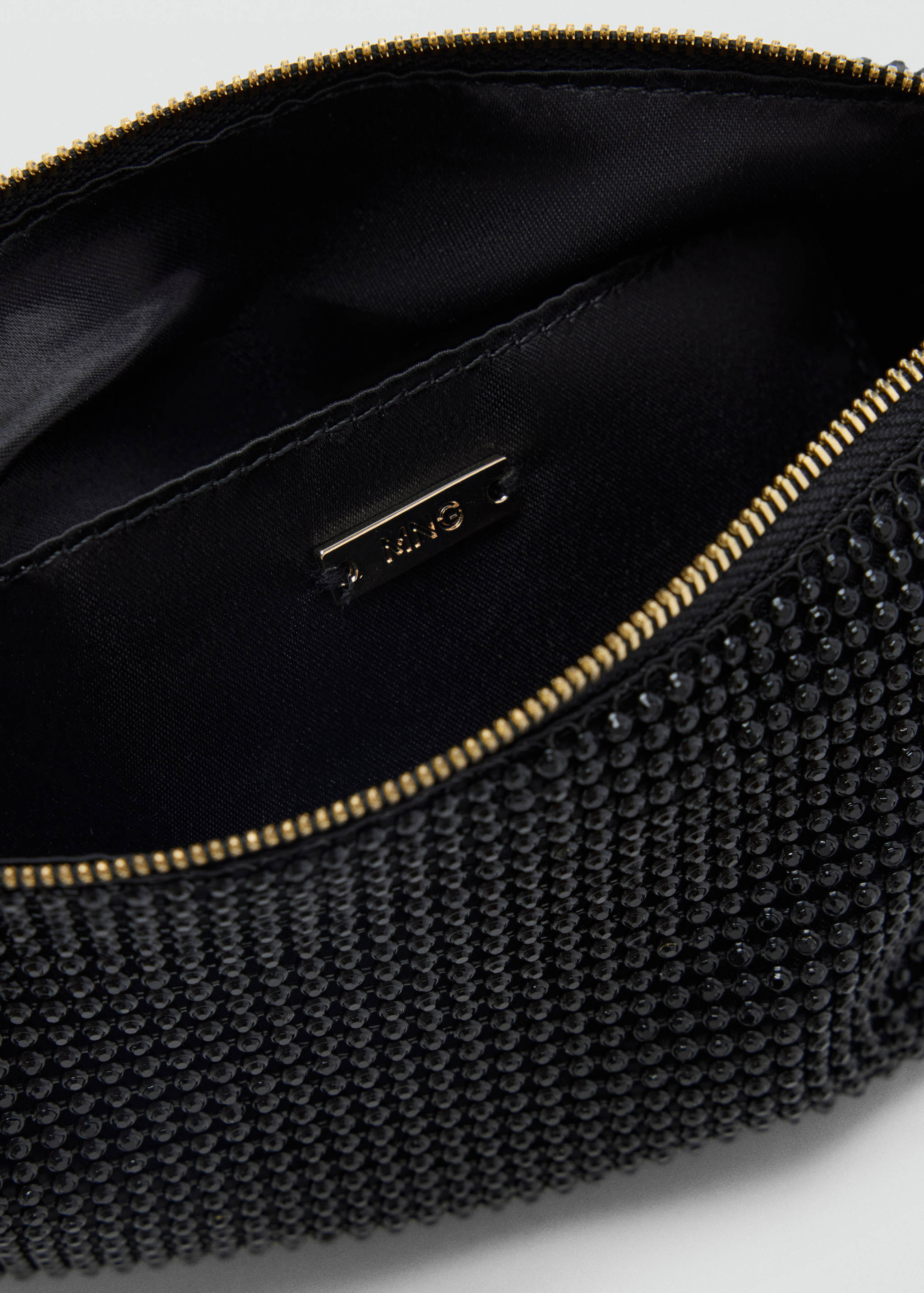 Black rhinestone handbag interior with gold zip and inner pocket detail.