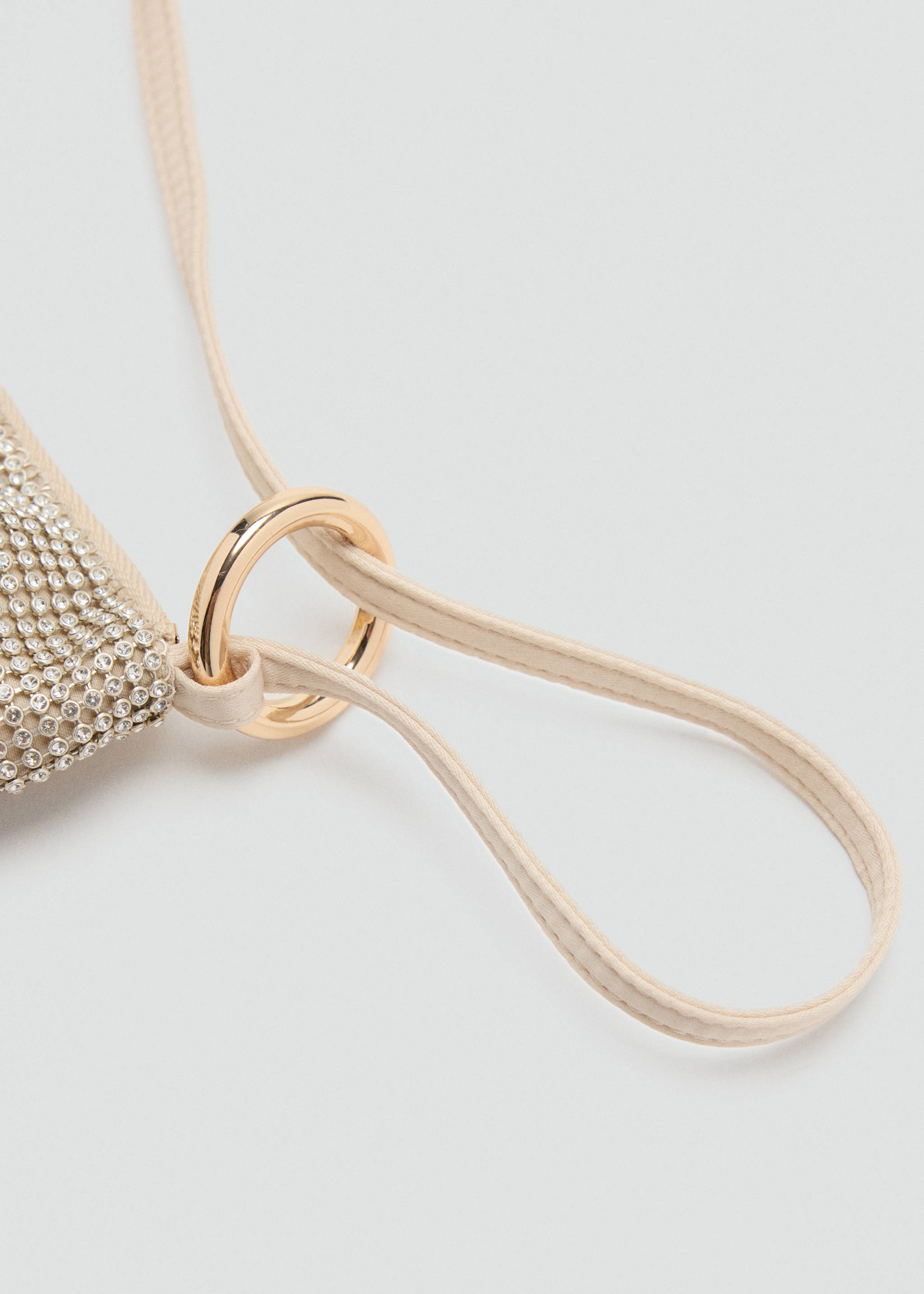 Close-up of a beige rhinestone handbag detail with a gold-tone metal ring and strap.