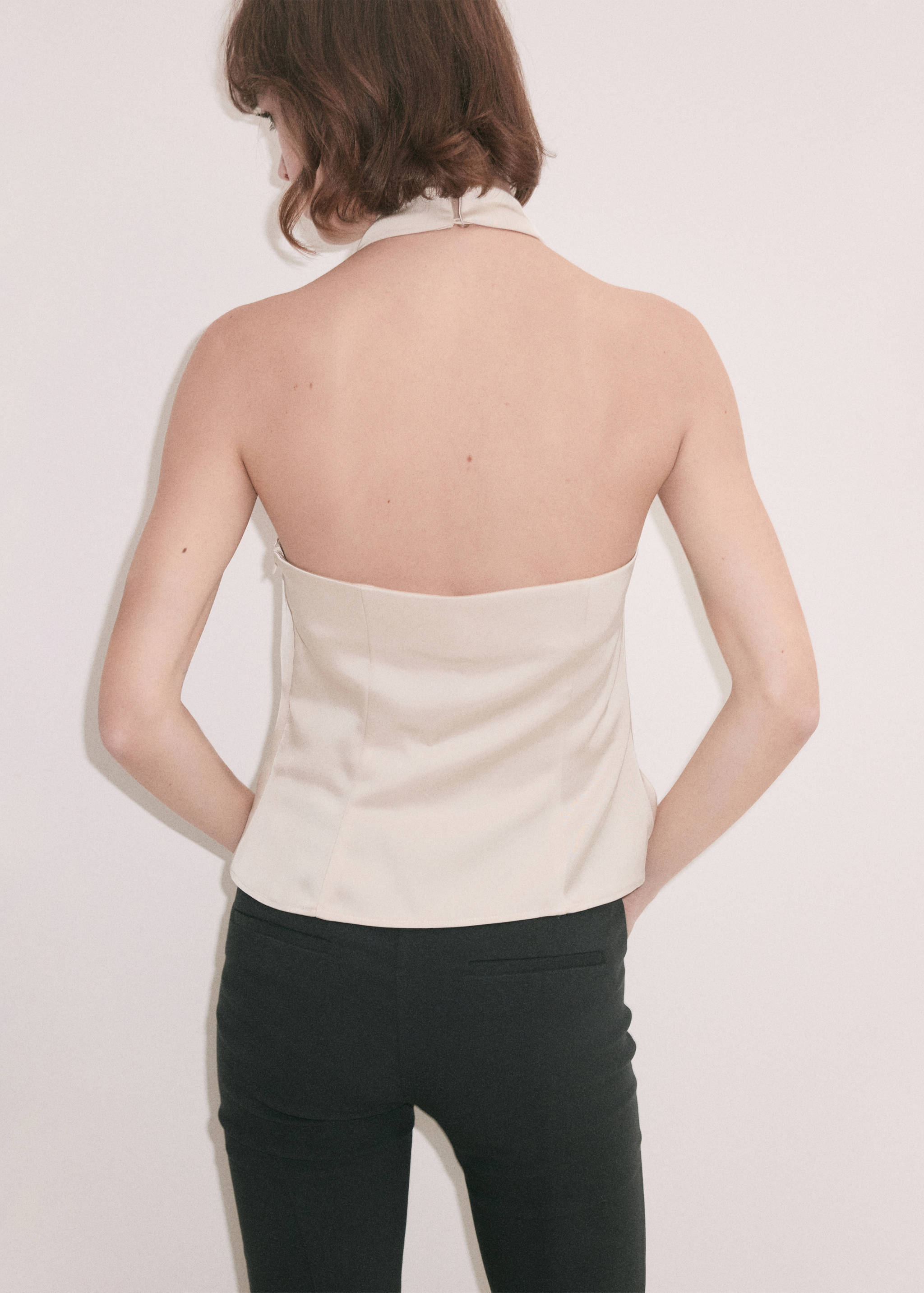 Cream halterneck top seen from the back, paired with dark trousers.
