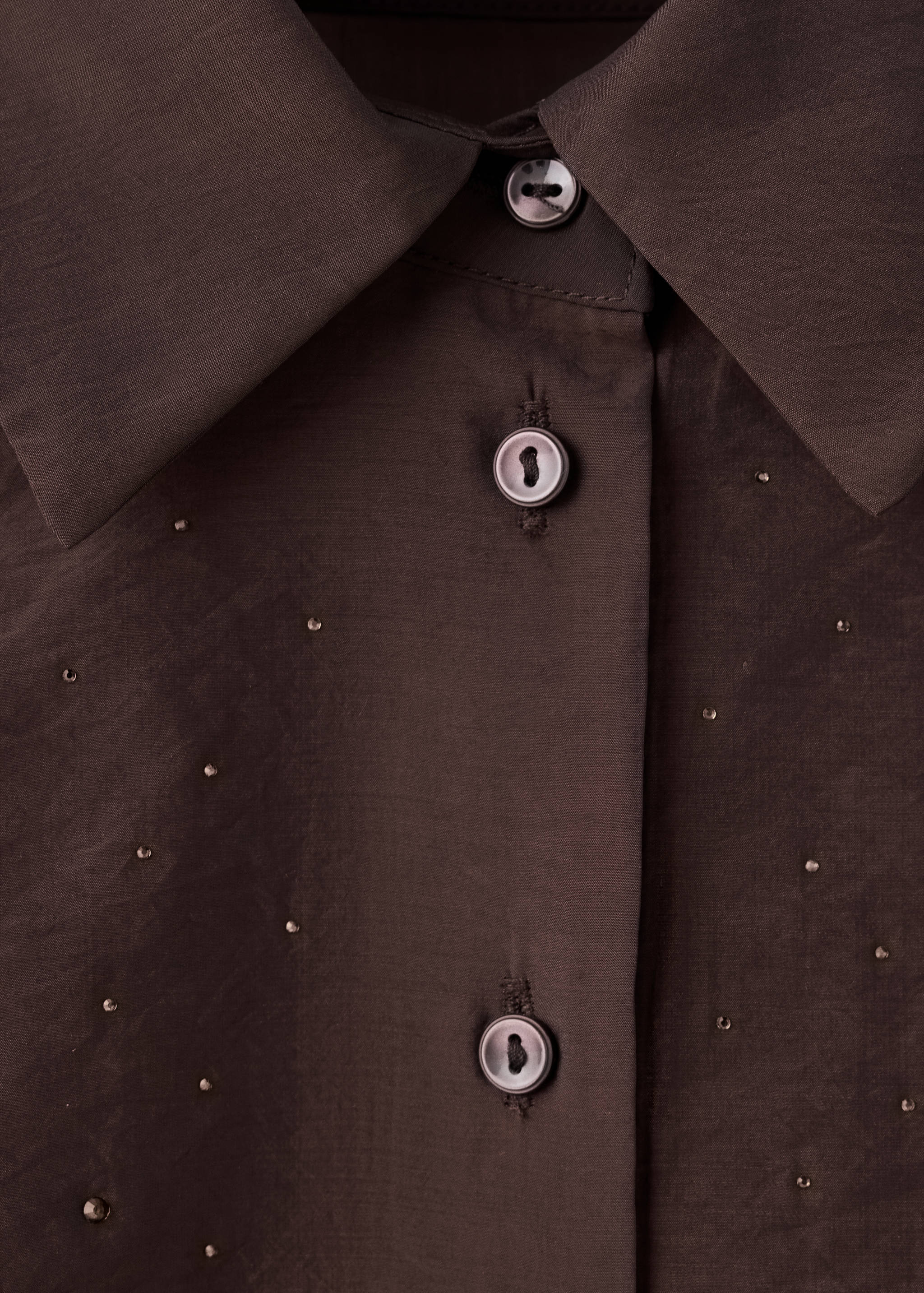 Dark brown shirt detail with a collar and metallic stud embellishments.