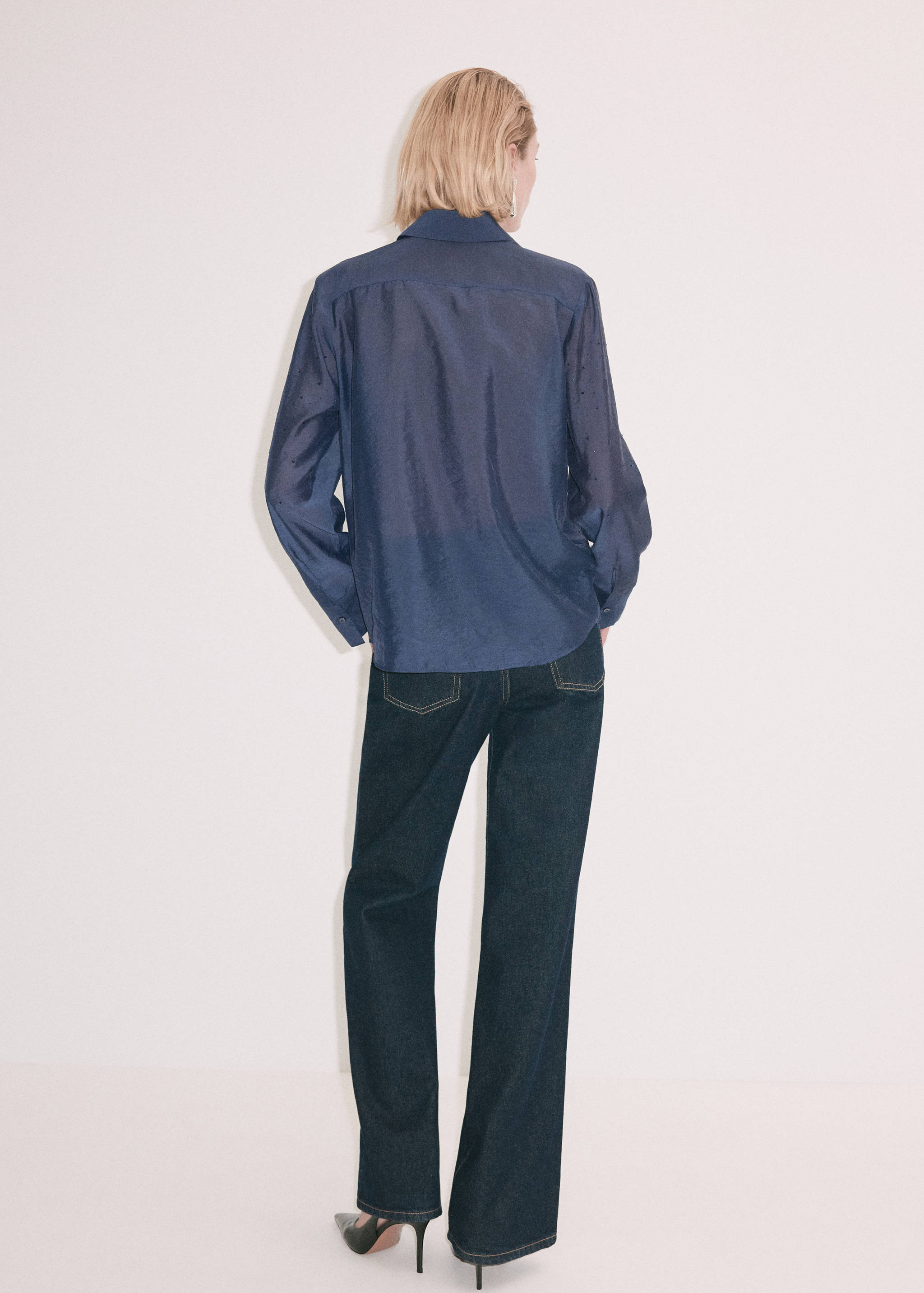 Back view of a dark blue shirt with long sleeves and a collar, worn with dark trousers.