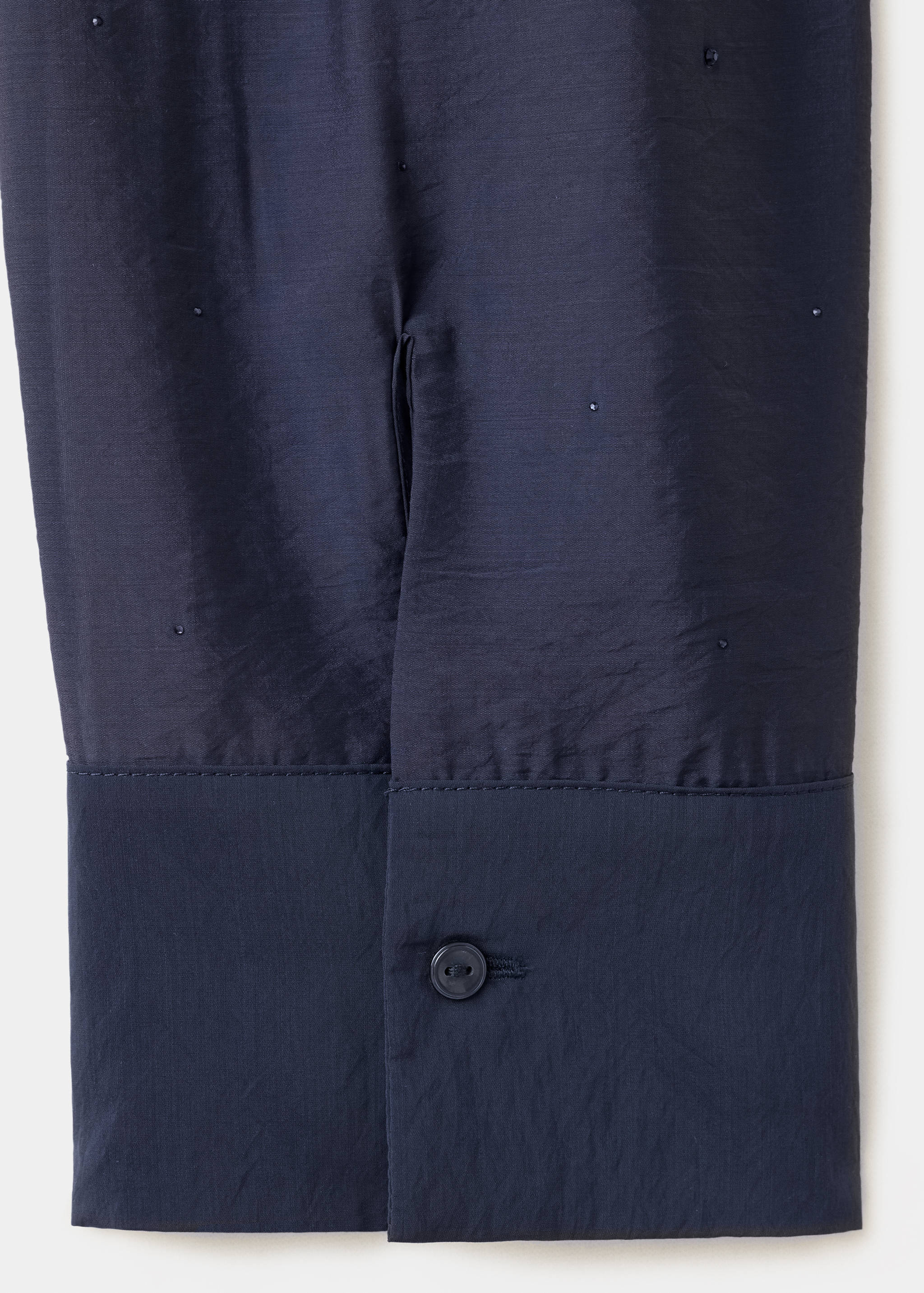 Close-up of a dark navy blue shirt cuff and beaded fabric texture.