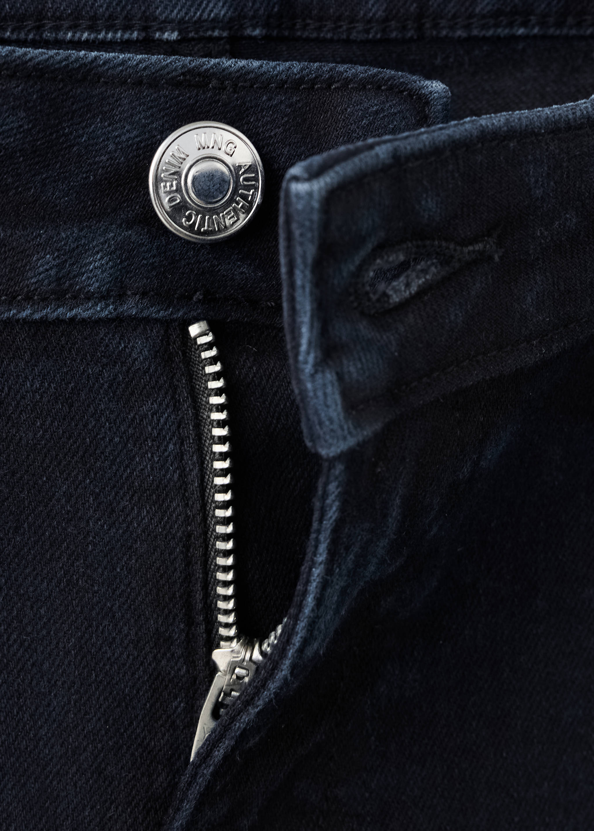 Close-up of dark blue denim jeans showing the metallic button and zipper fly detail.