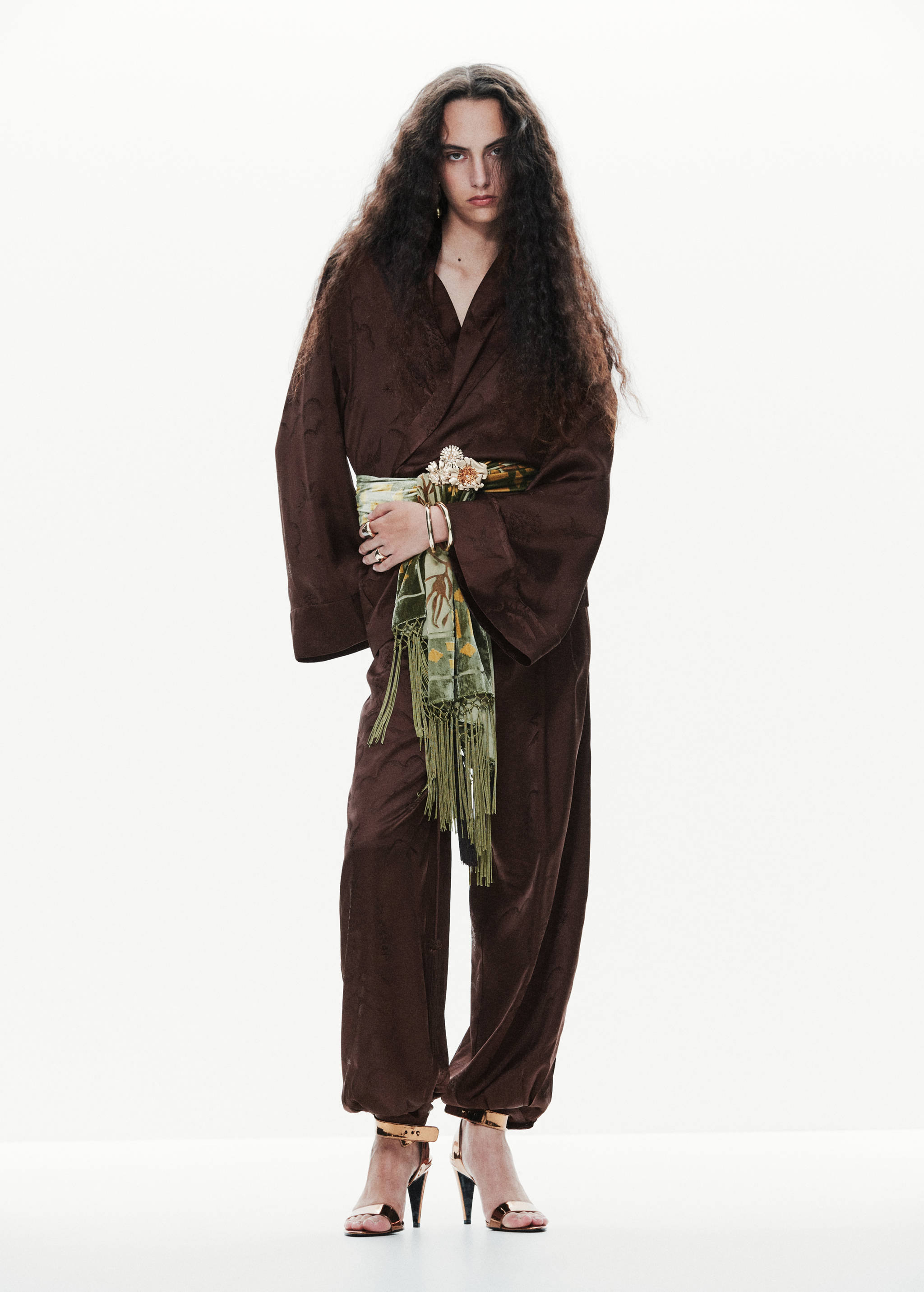 Dark brown patterned blazer with wide sleeves and matching trousers, worn with a fringed olive scarf.