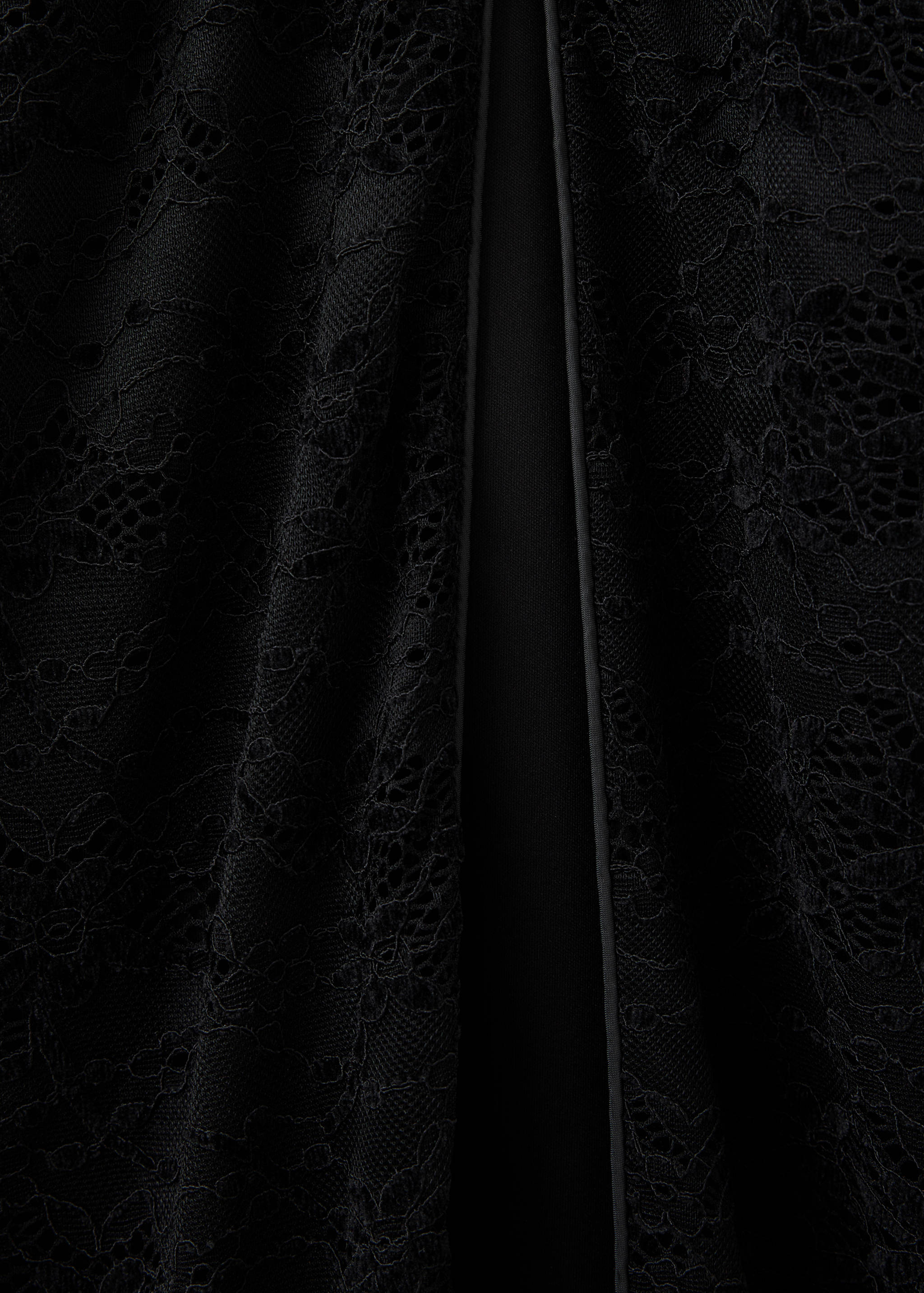 Close-up of black lace dress fabric with a vertical piped split.