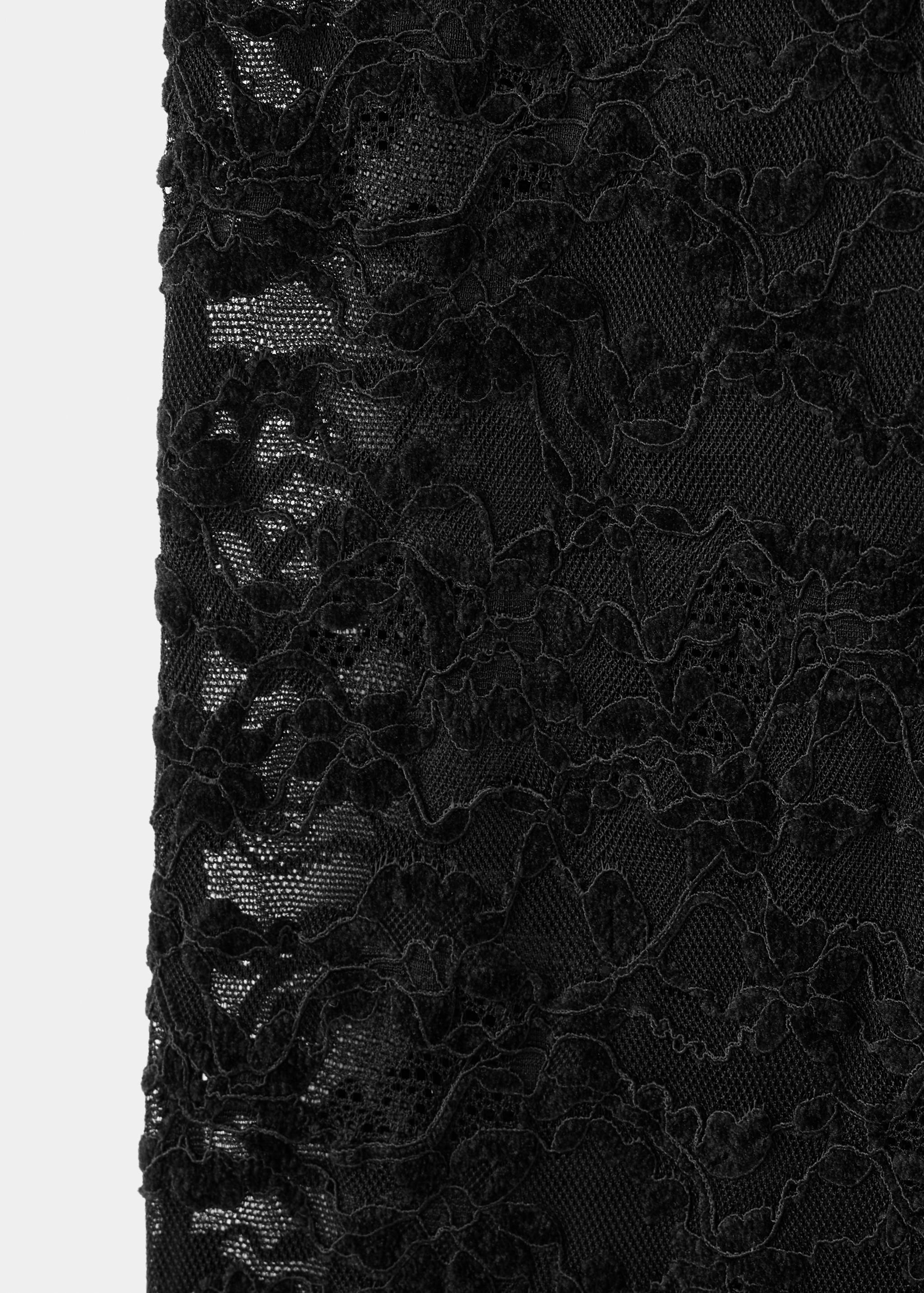 Black lace fabric detail of trousers showing a floral pattern and sheer mesh.