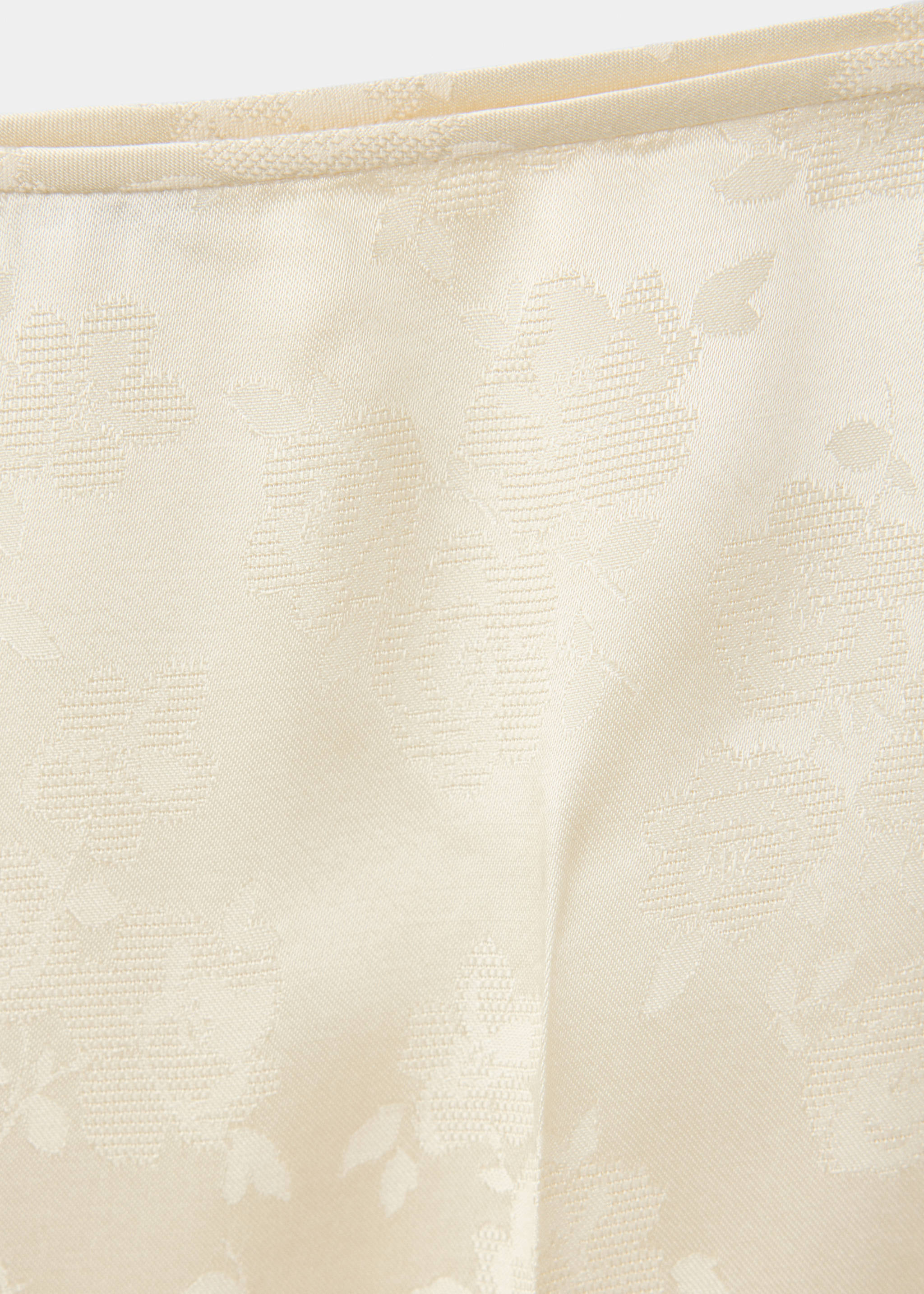 Close-up of cream trousers featuring a tonal floral jacquard fabric texture.