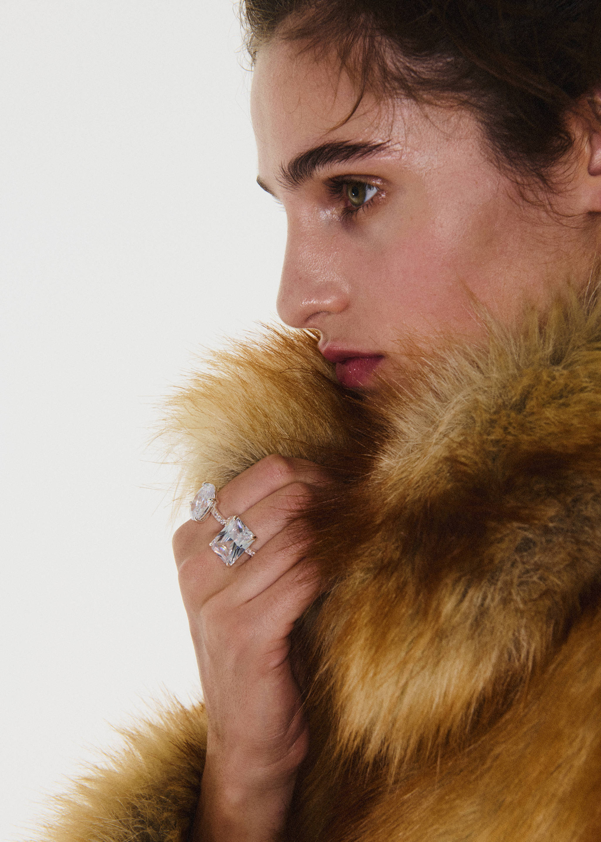 Silver rings with large crystal stones worn on a model's hand near a faux-fur coat.