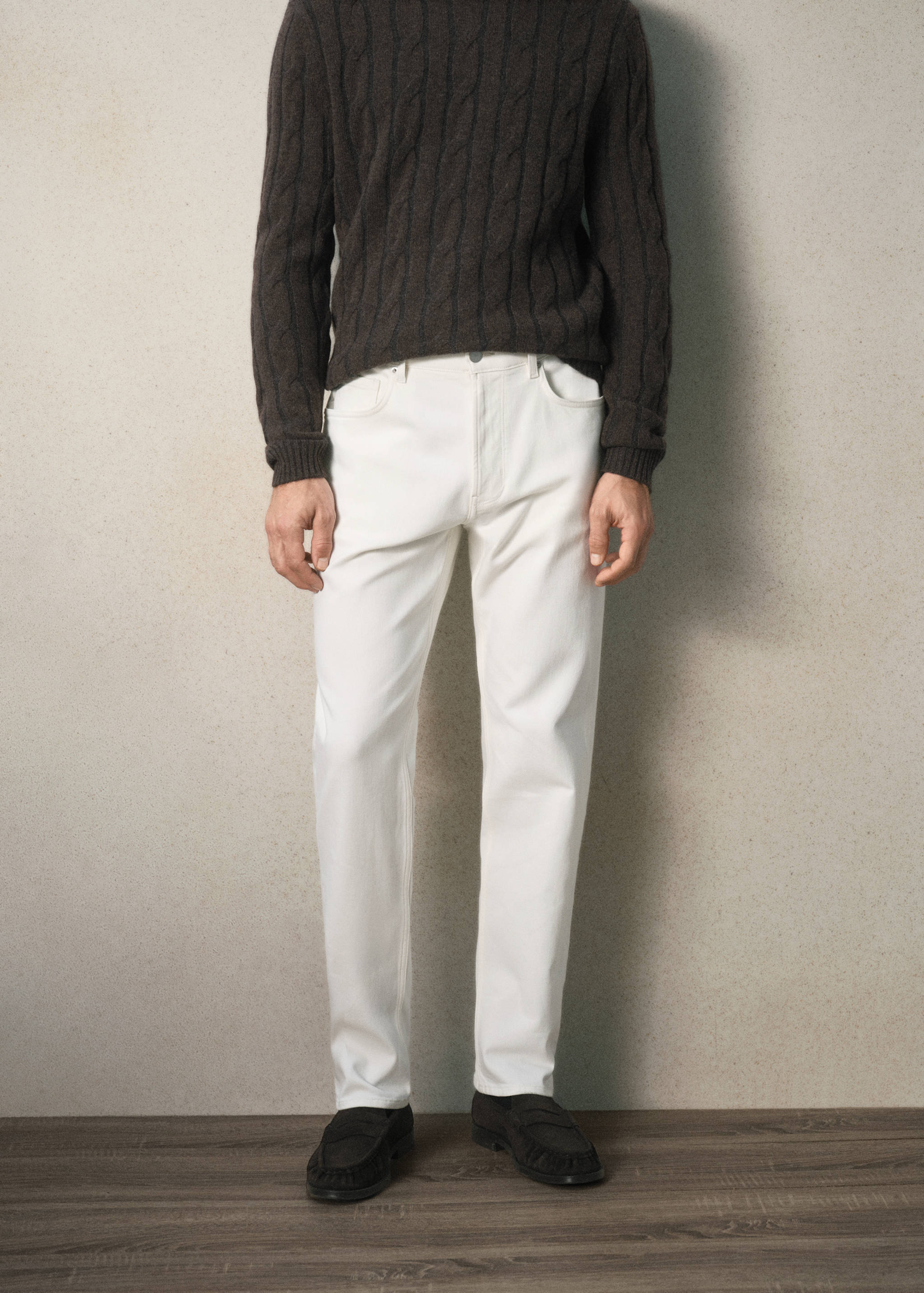 White denim trousers styled with a dark brown cable-knit jumper.