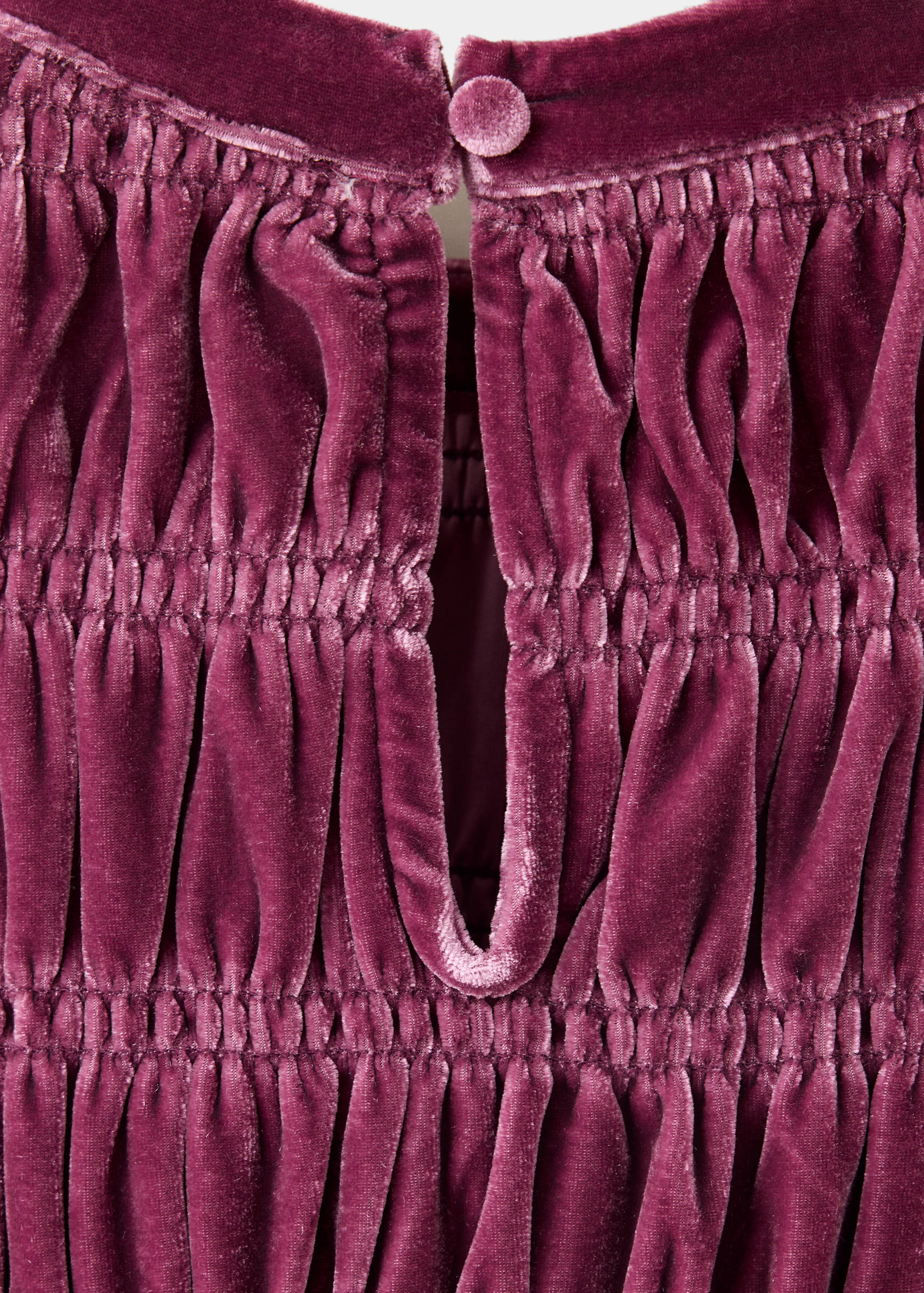 Close-up of plum velvet dress fabric showing gathered bodice and back button.
