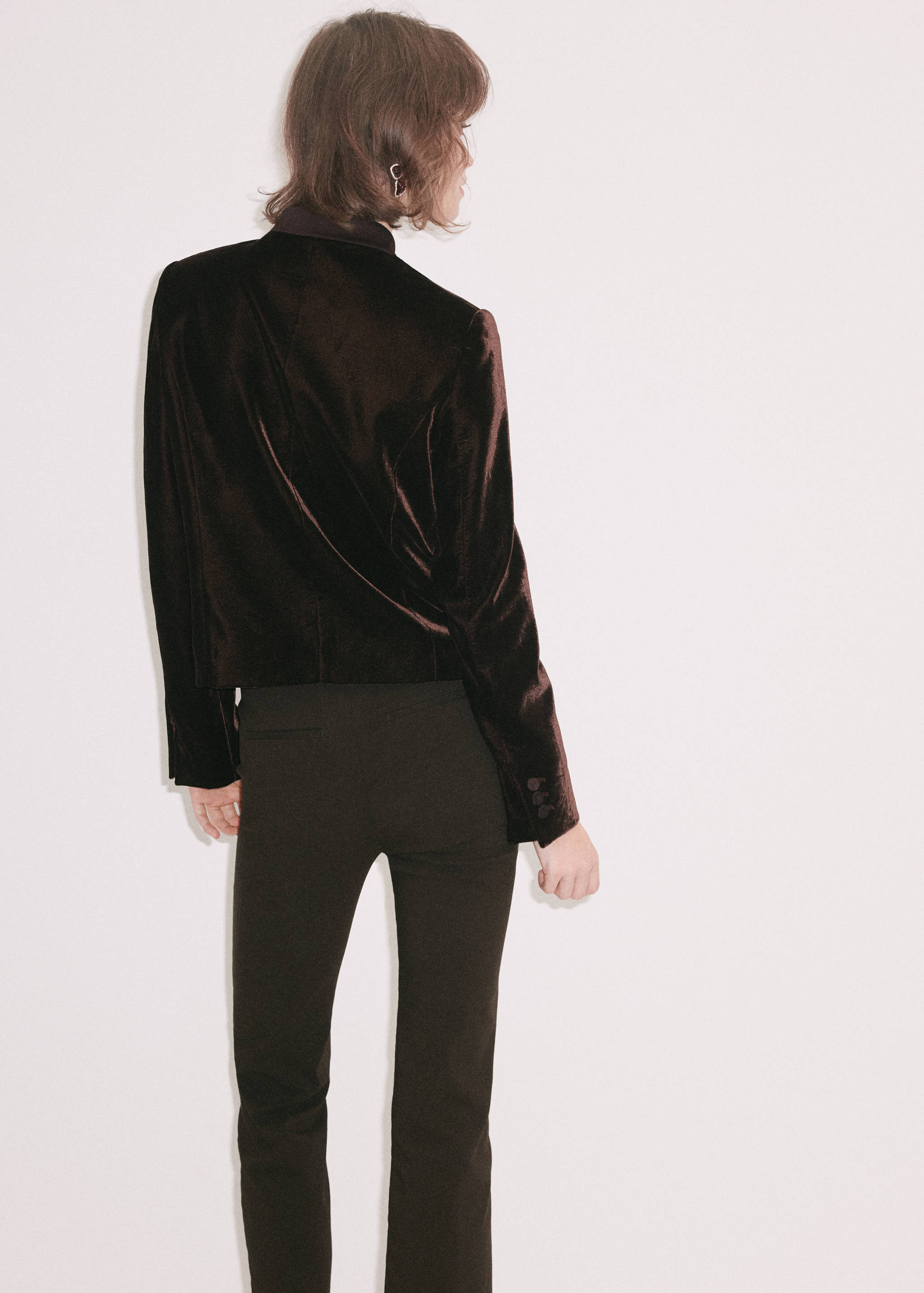 Blazer de terciopelo marrón oscuro visto de espaldas, con silueta entallada y hombros estructurados.