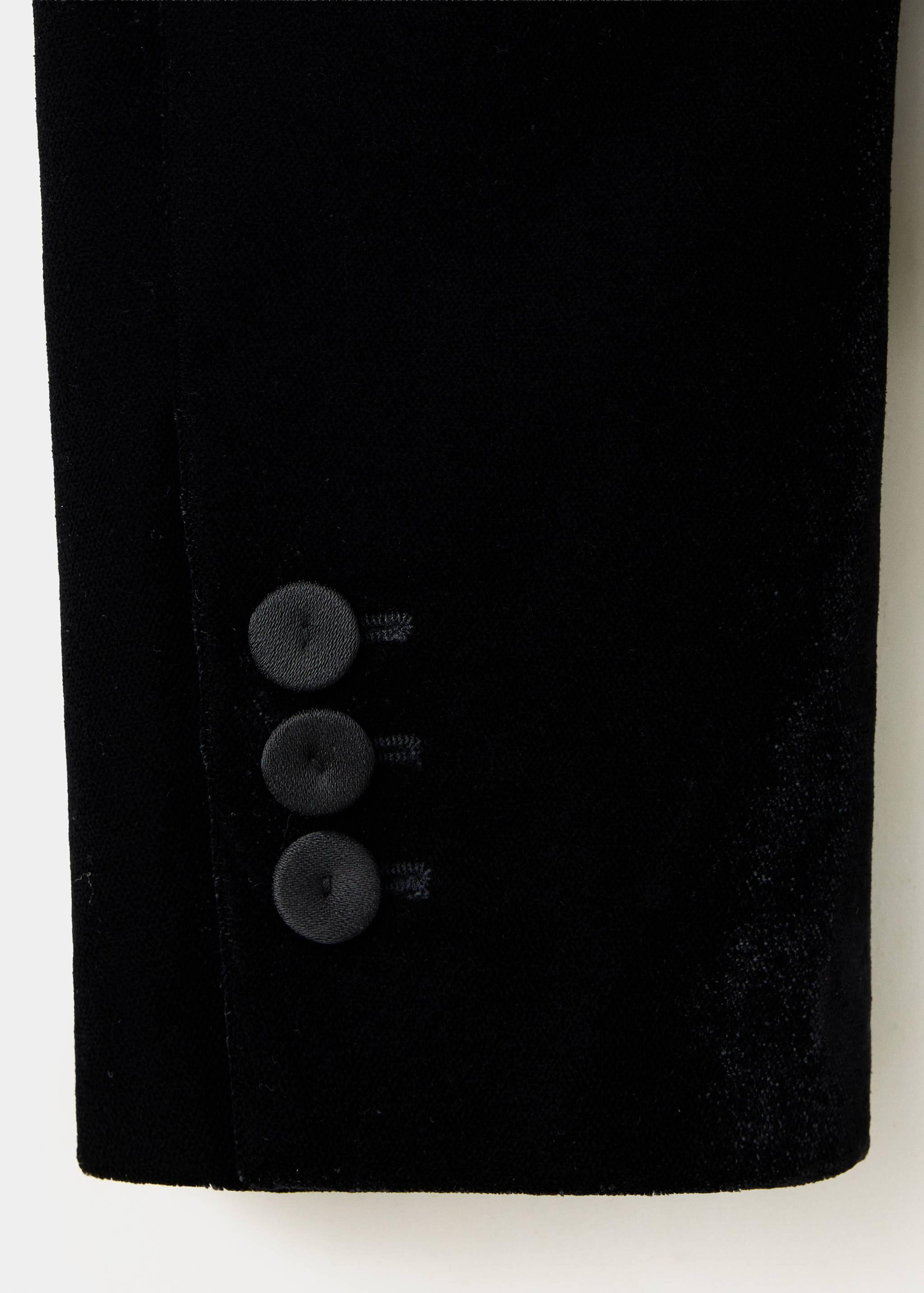 Detalle del puño de una chaqueta americana negra de terciopelo con tres botones.
