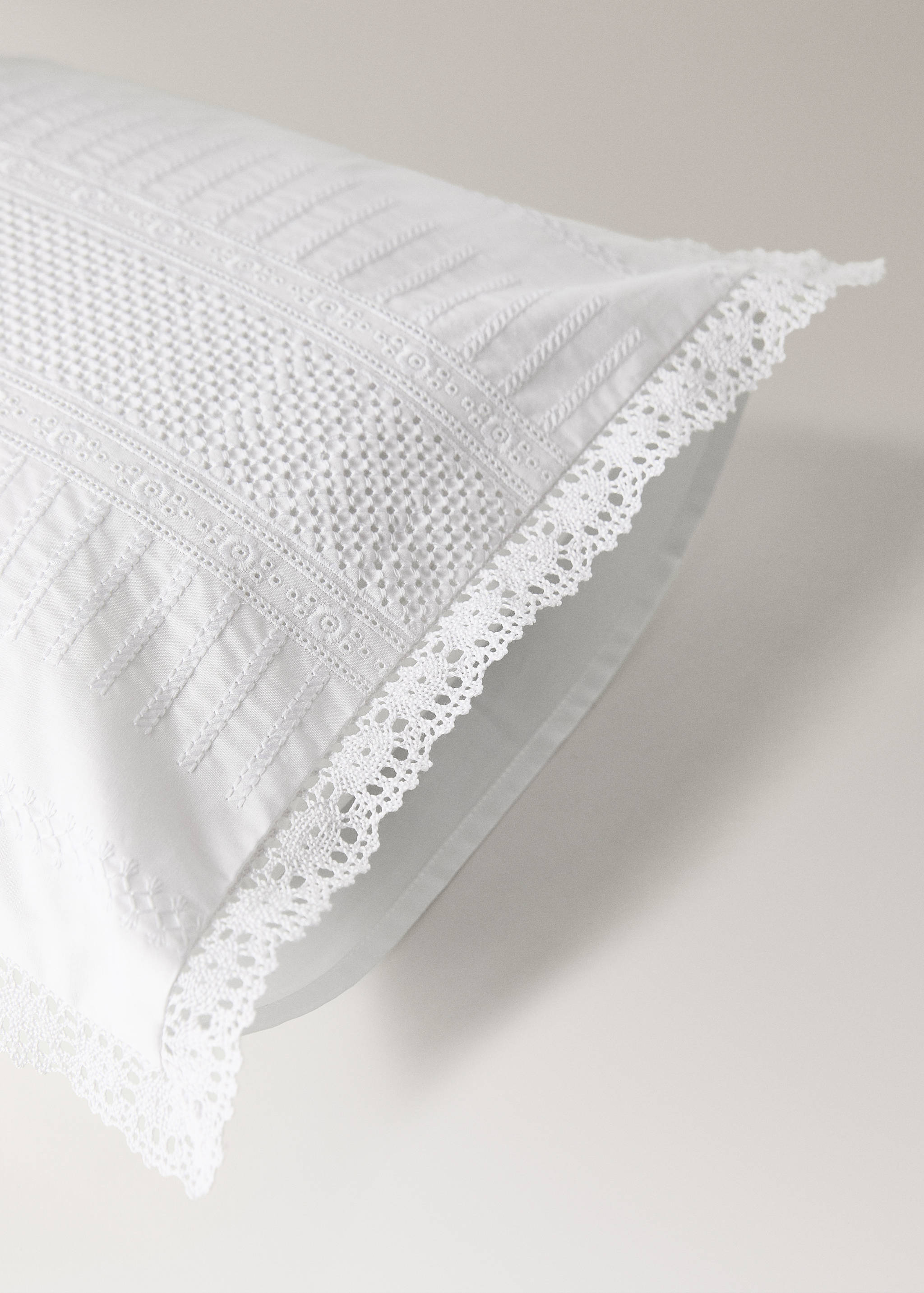 White cushion cover with intricate embroidered panels and lace trim.