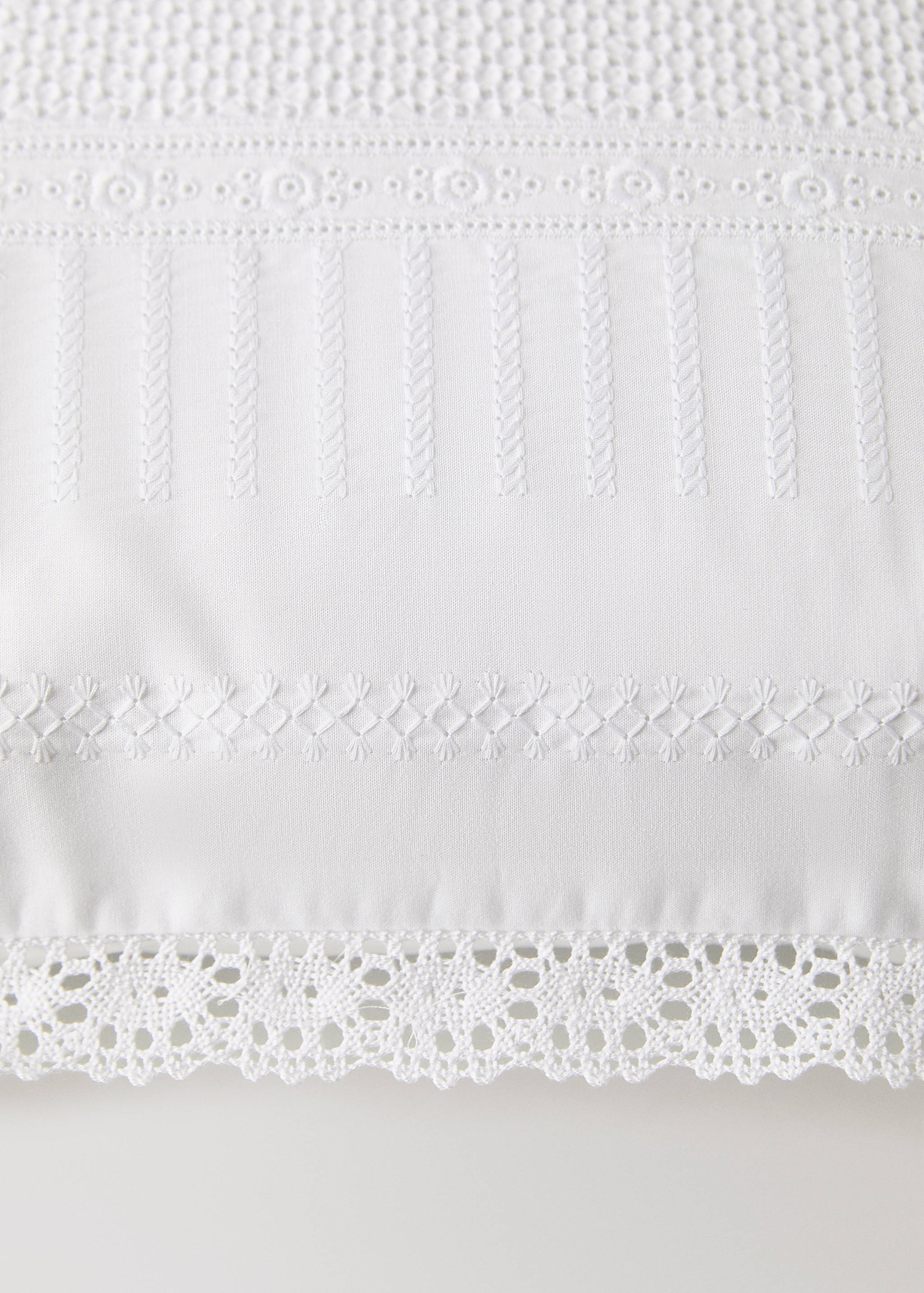 White cushion cover with embroidered details and lace border.