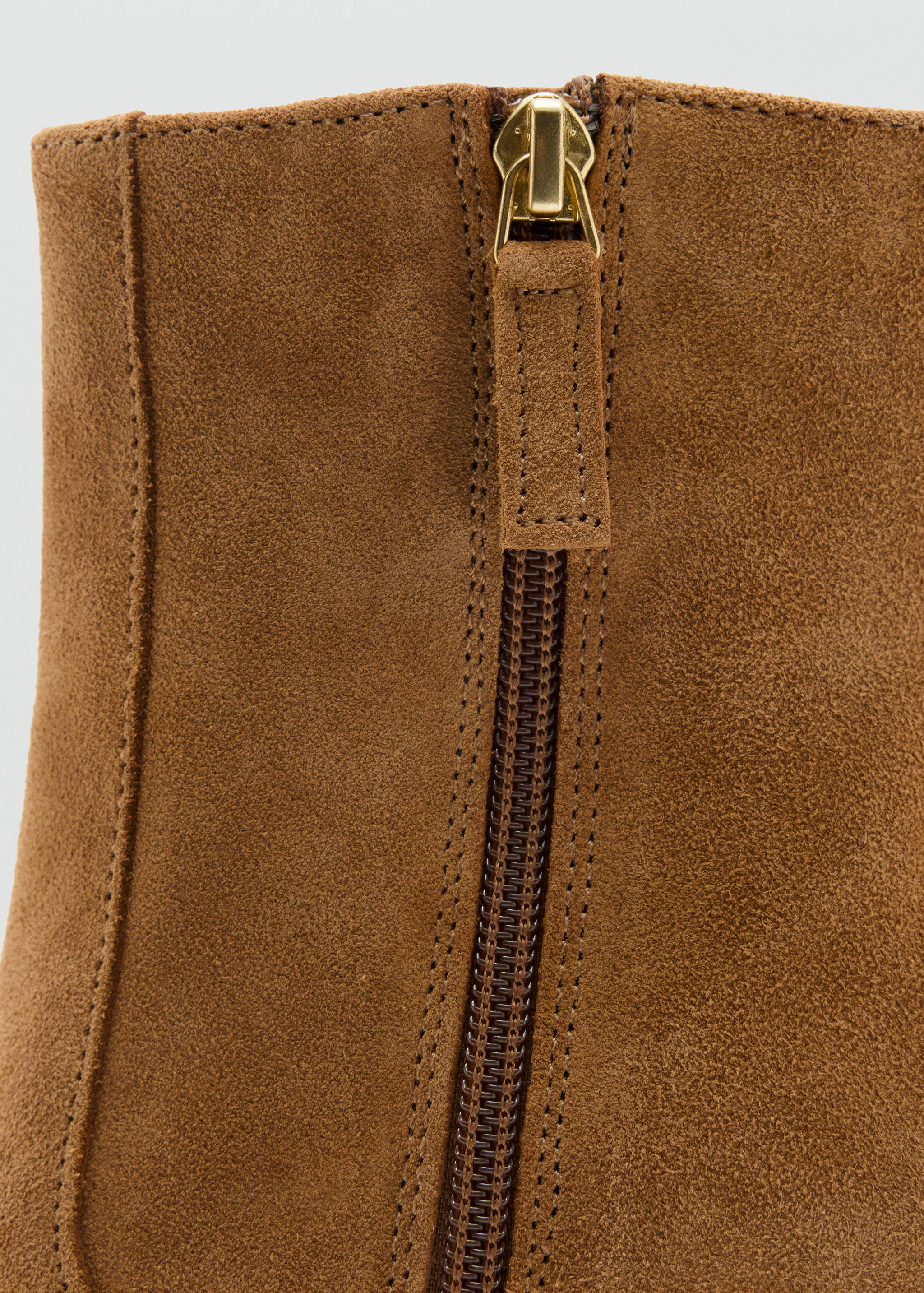 Close-up of the gold-toned zipper detail on brown suede ankle boots.