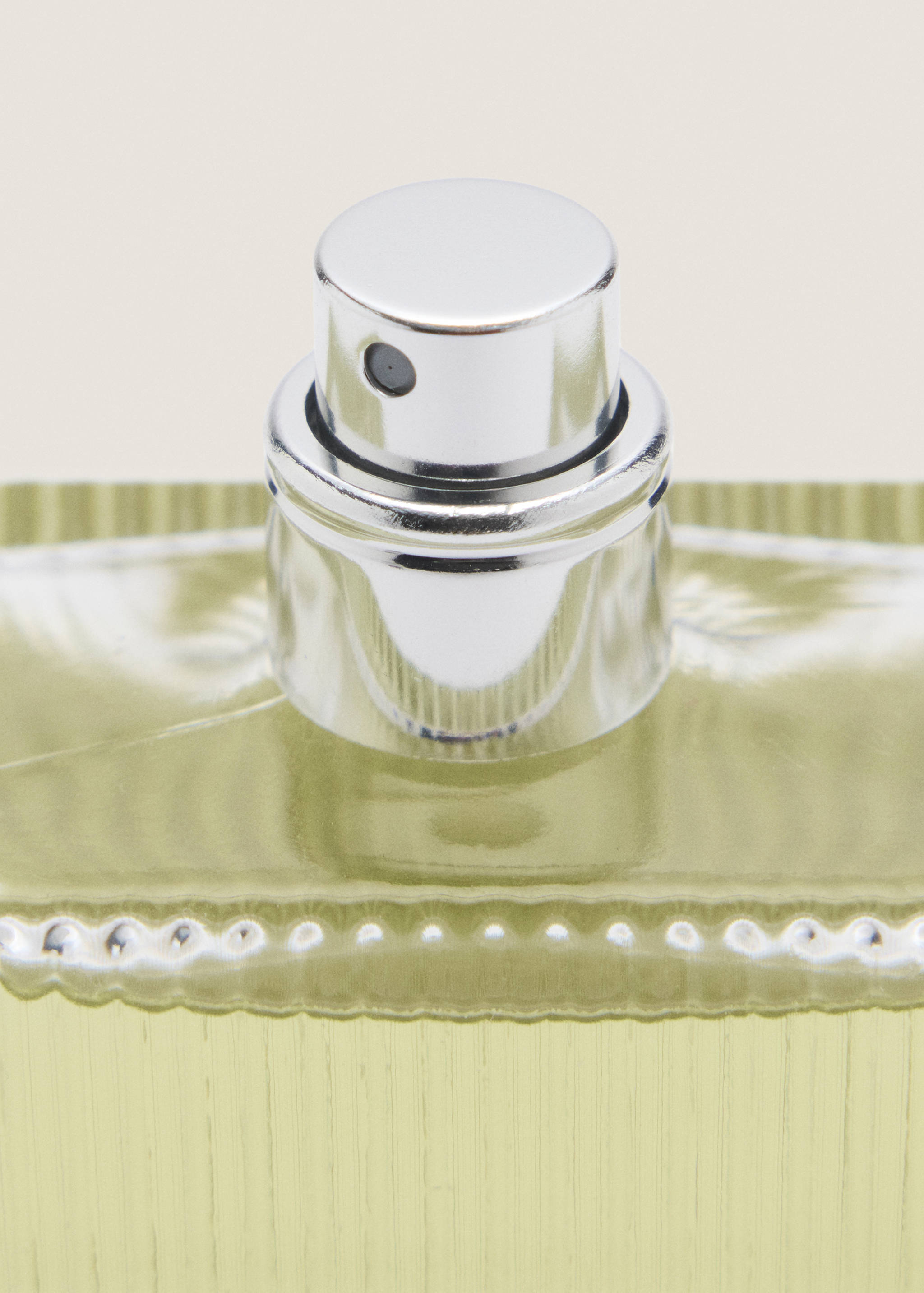 Close-up of a pale green perfume bottle with a silver spray nozzle and cap.